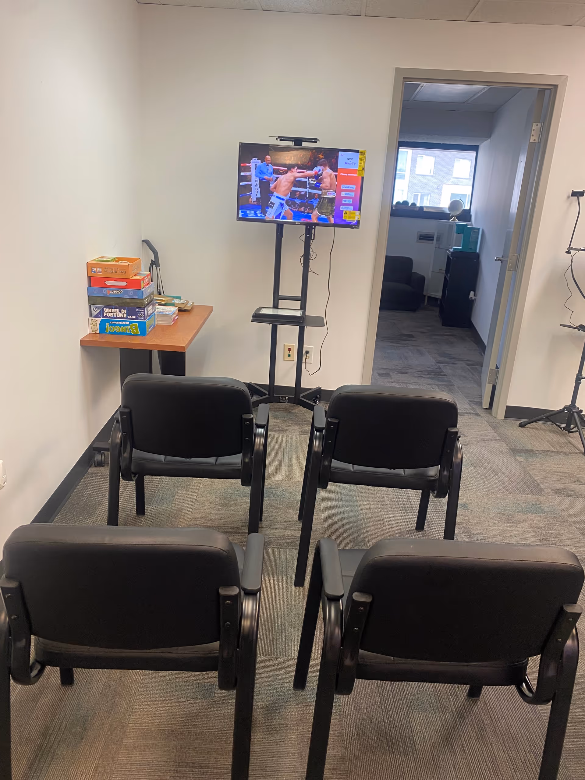 Small lounge with black chairs facing a TV on a stand and a game table.