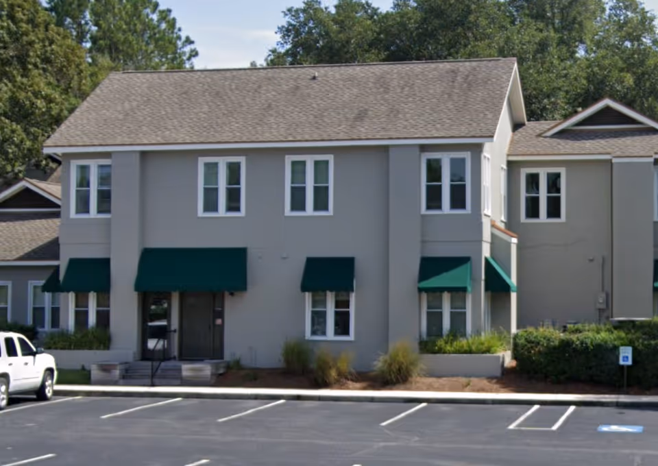 Front exterior of a senior living building with beige walls and green awnings.