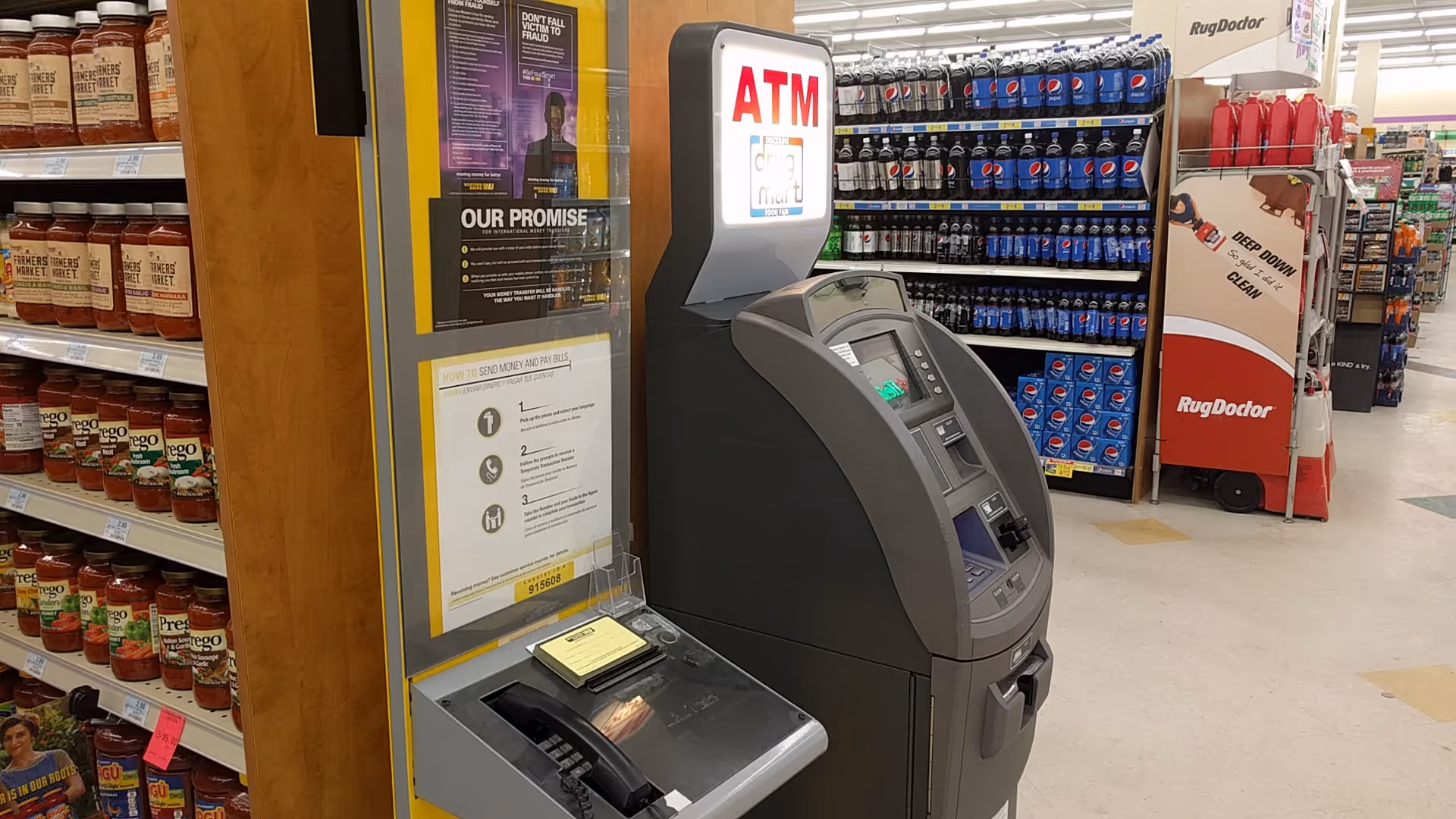 Inside a Discount Drug Mart store, an ATM kiosk sits near beverage shelves.