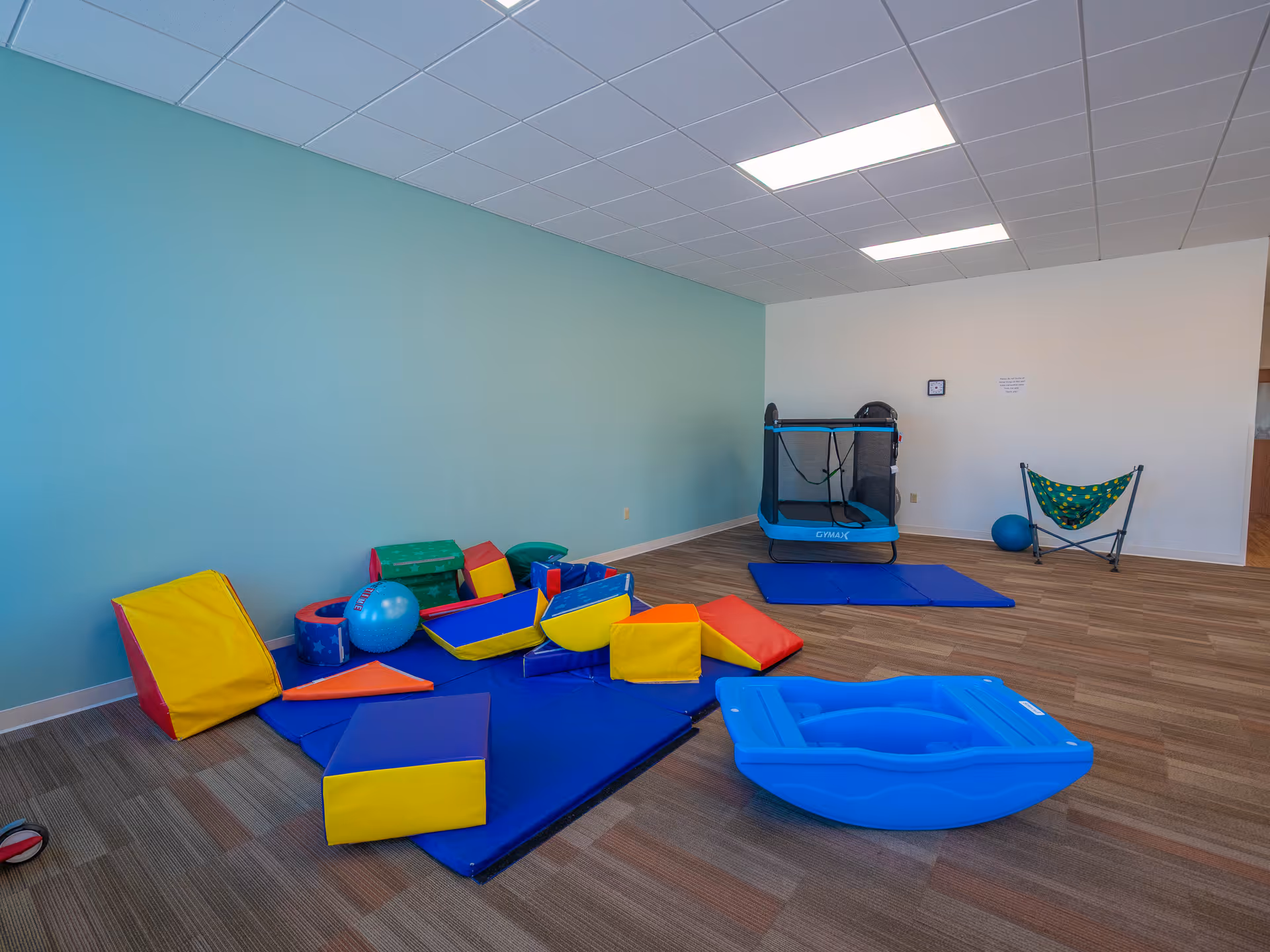Bright playroom with blue walls, foam toys, mats, and a small trampoline.
