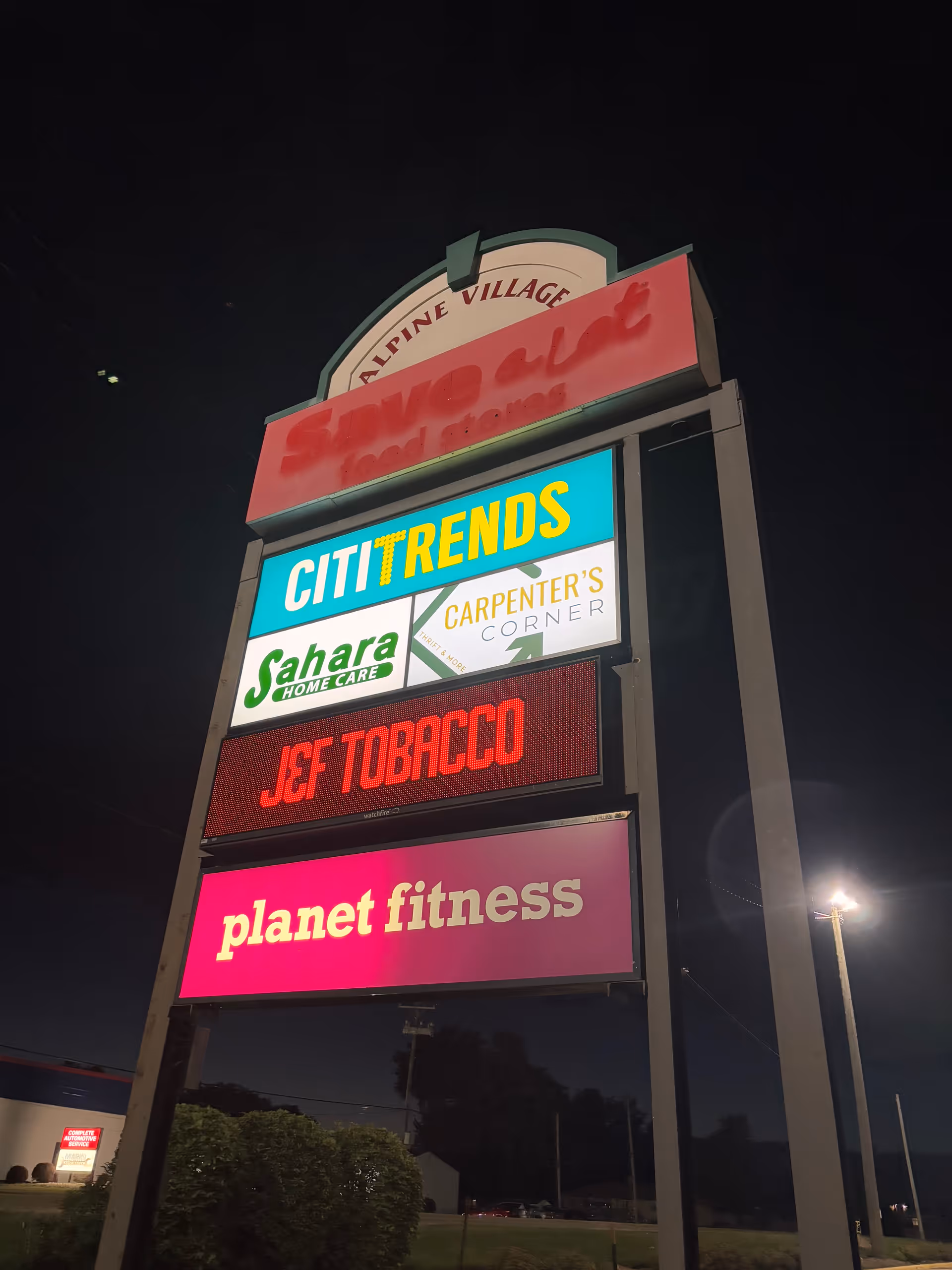 Nighttime exterior signboard listing Sahara Home Care among other stores.