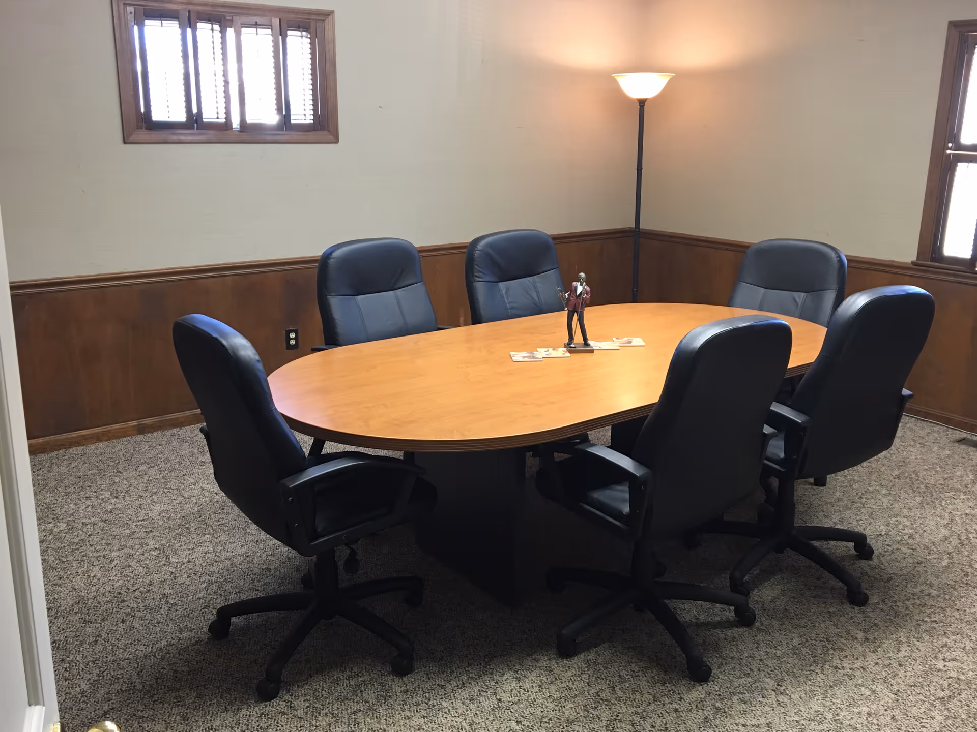 A round wooden conference table with eight black office chairs in a warmly lit meeting room.