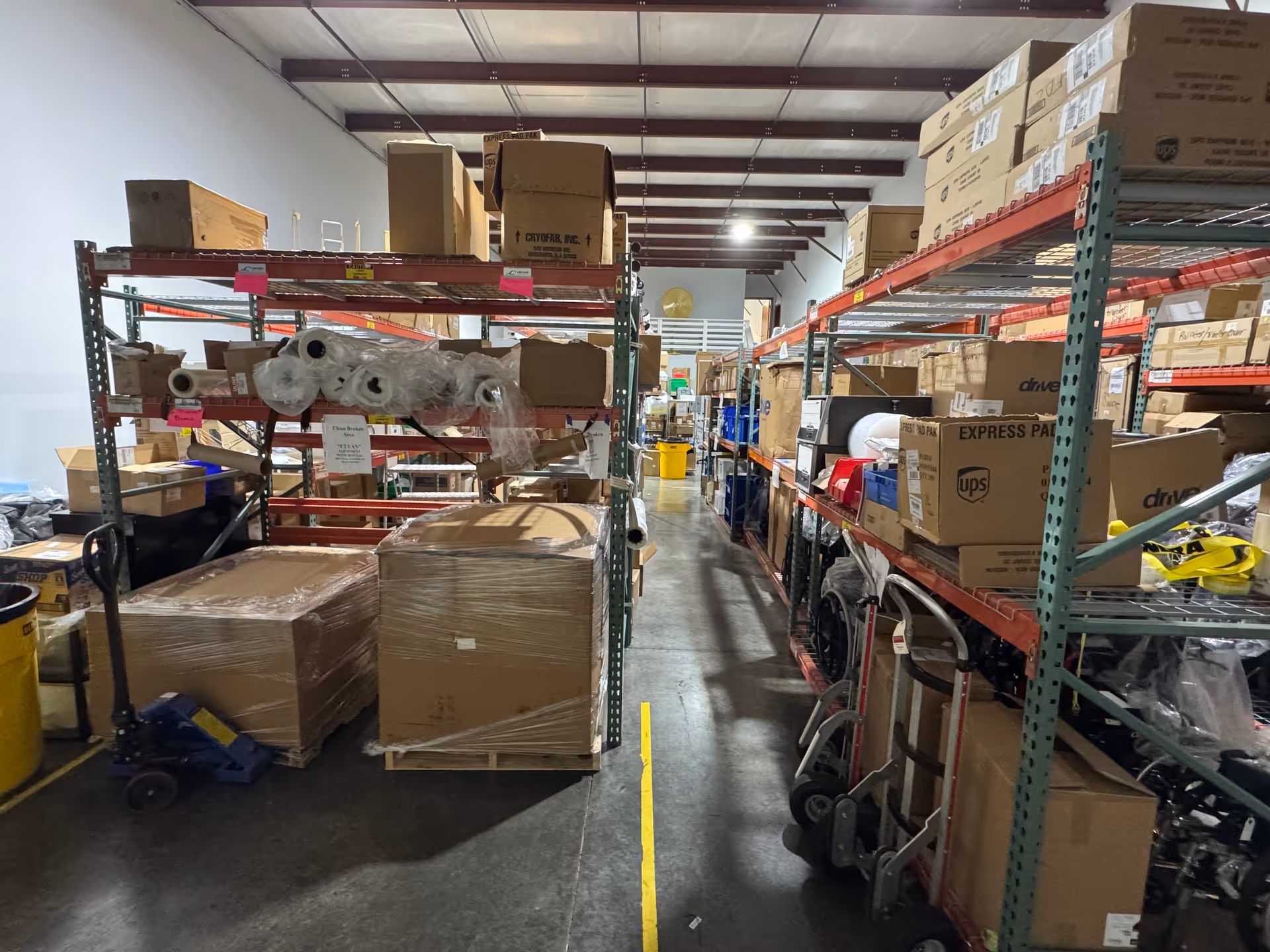 Interior warehouse aisle with metal shelving, pallets, and packed boxes in storage area.