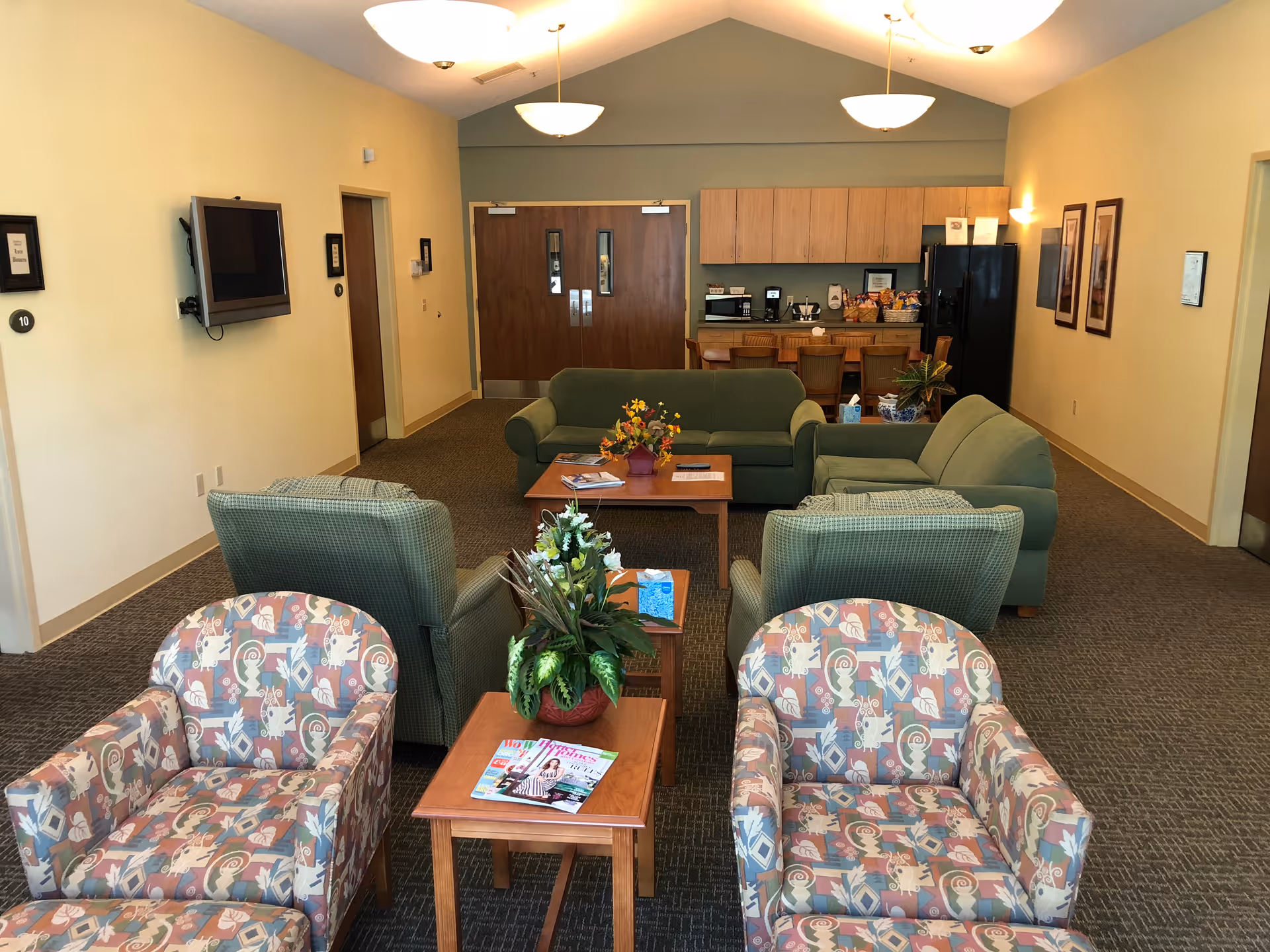Lounge area with green sofas, patterned chairs, and tables in a facility common room.