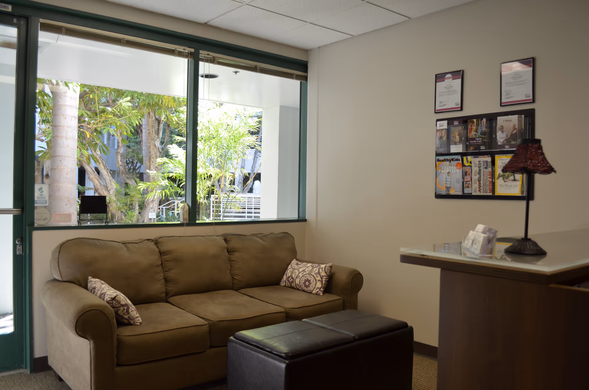 Cozy beige lounge area with a brown sofa, window view, and a reception desk.