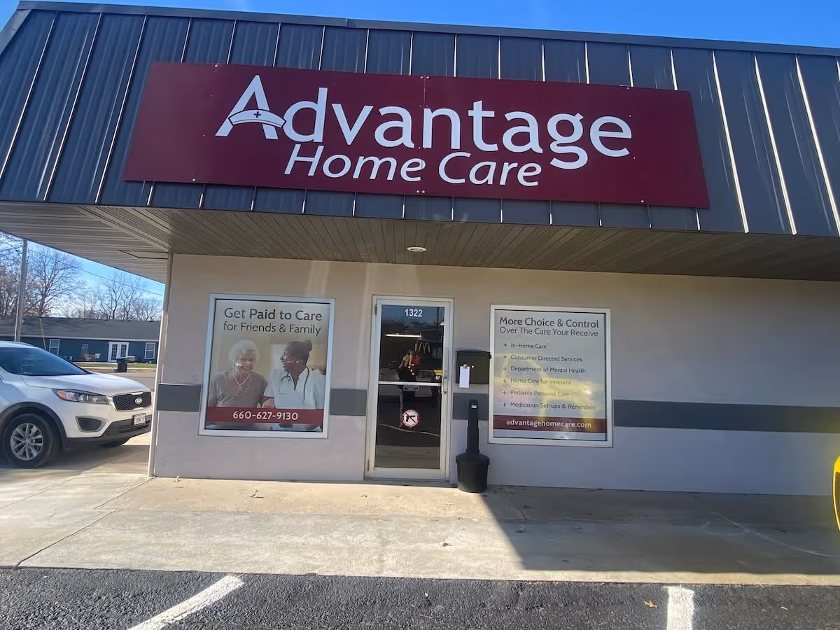 Front of Advantage Home Care storefront with maroon sign, glass doors, and posters in windows.