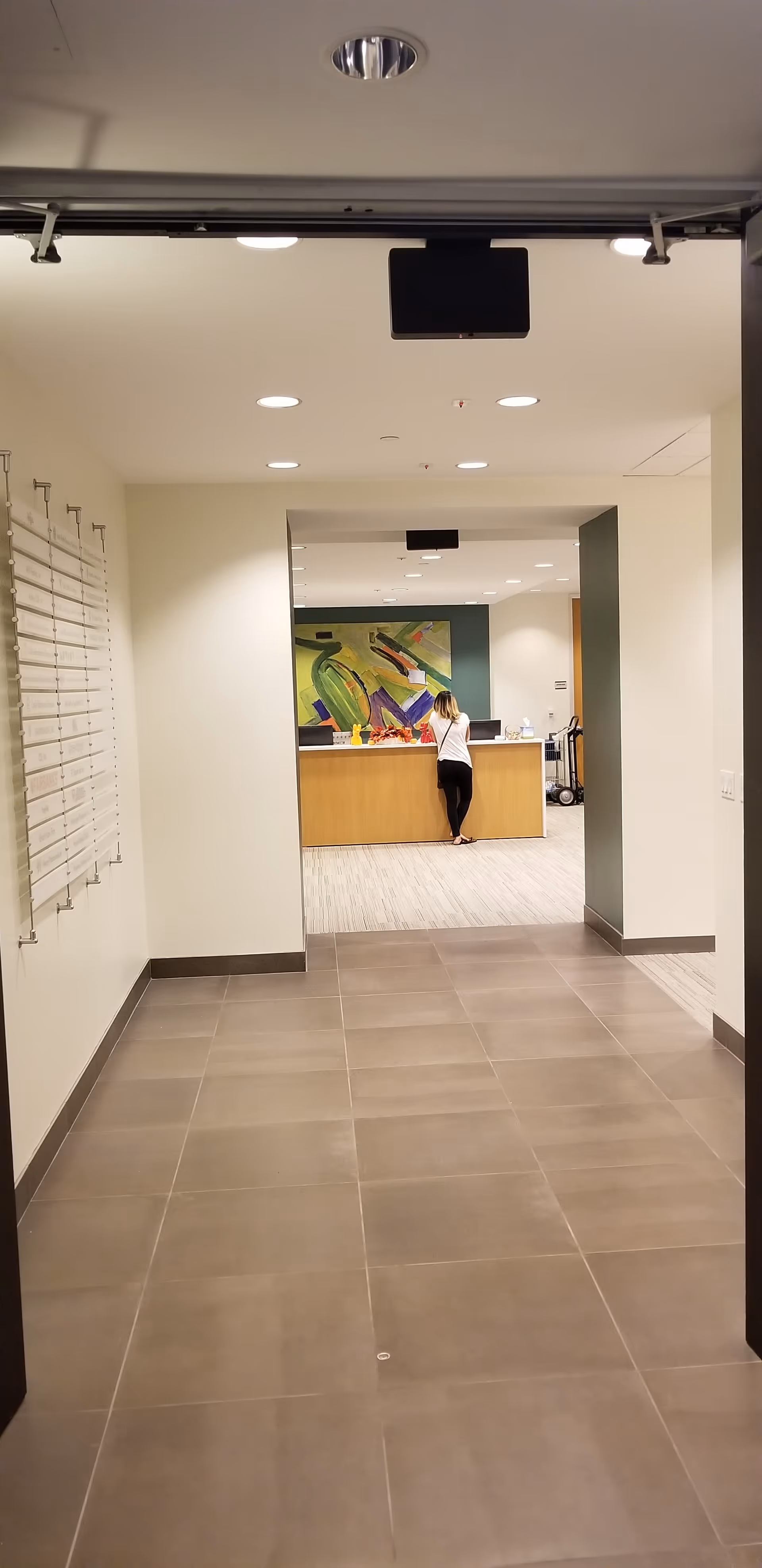 Long hallway leads to a reception desk with a colorful mural and a standing staff member.