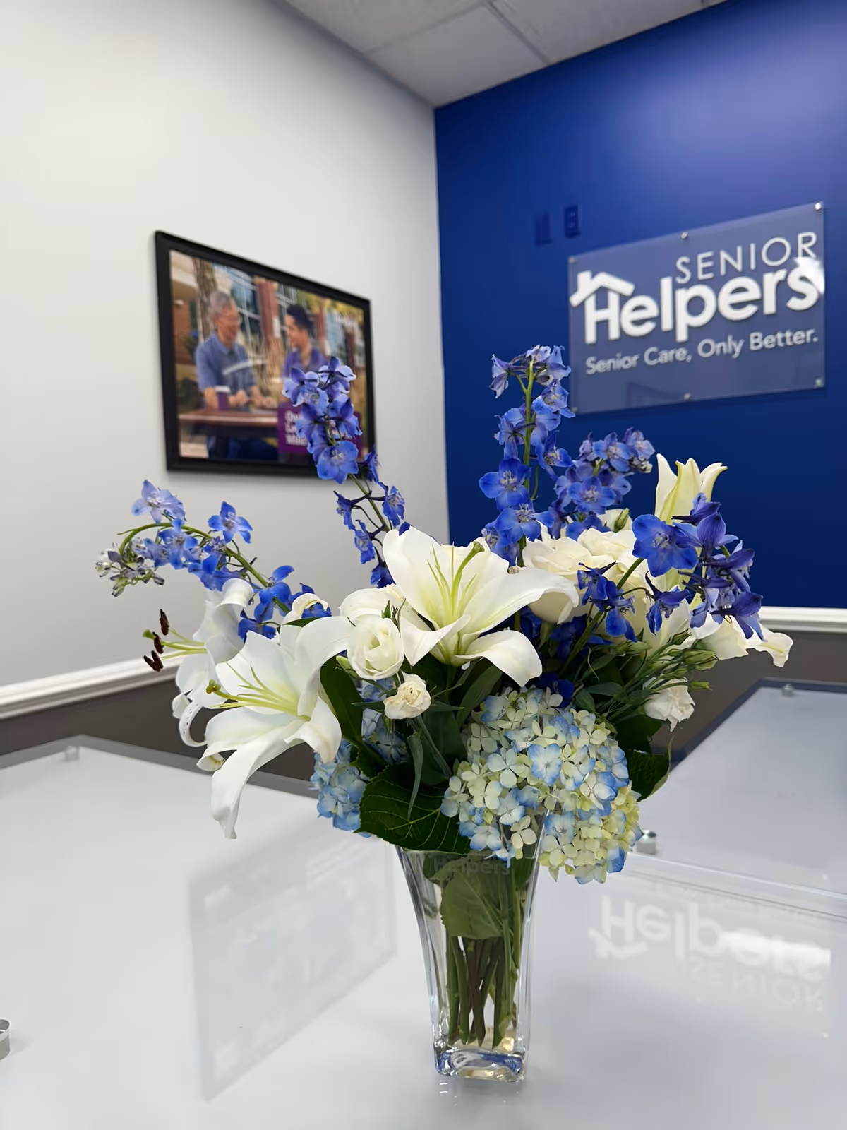 Blue and white bouquet in a glass vase on a white counter beside Senior Helpers sign