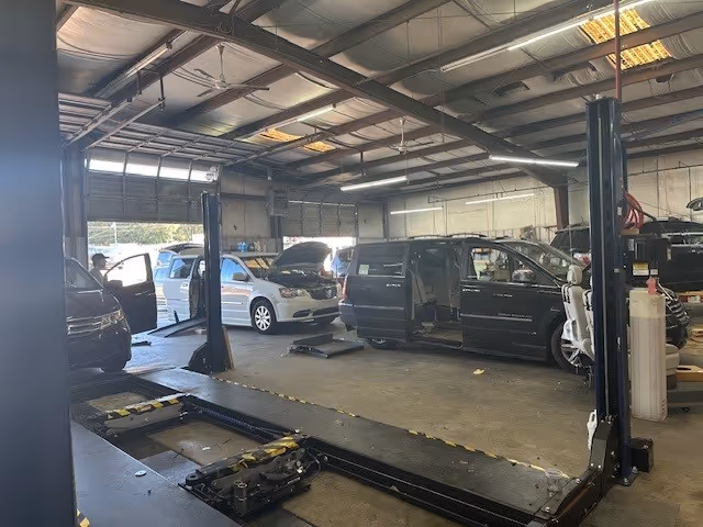 Indoor automotive workshop with multiple cars on lifts and equipment in a spacious bay.