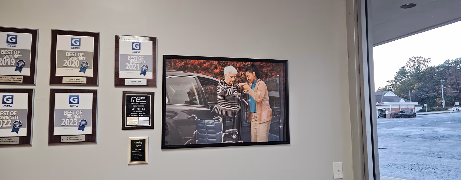 Interior wall with framed awards and a large photo of two elderly people near a window.