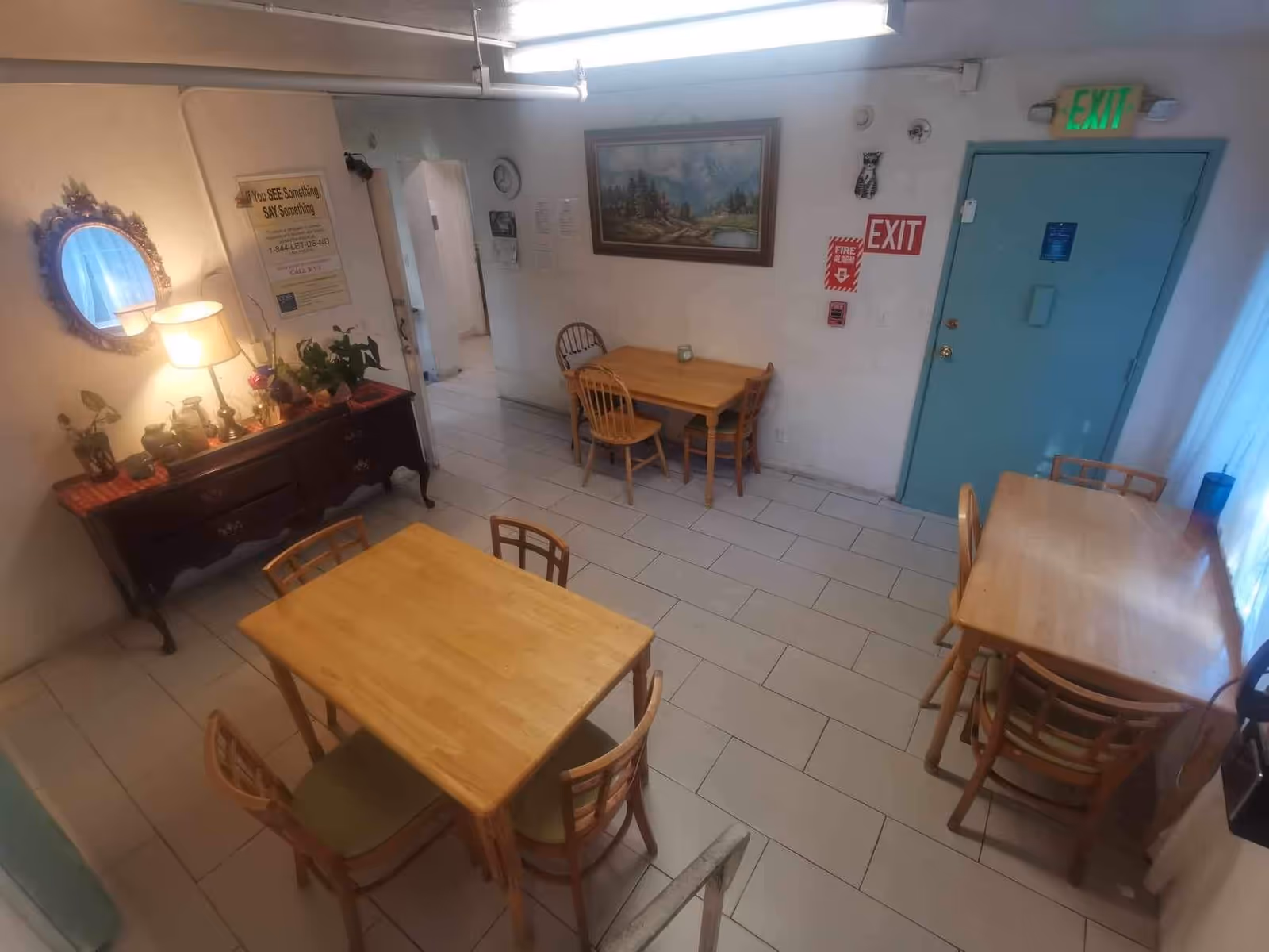 Indoor dining room with wooden tables and chairs, plants, wall art, and a blue exit door.