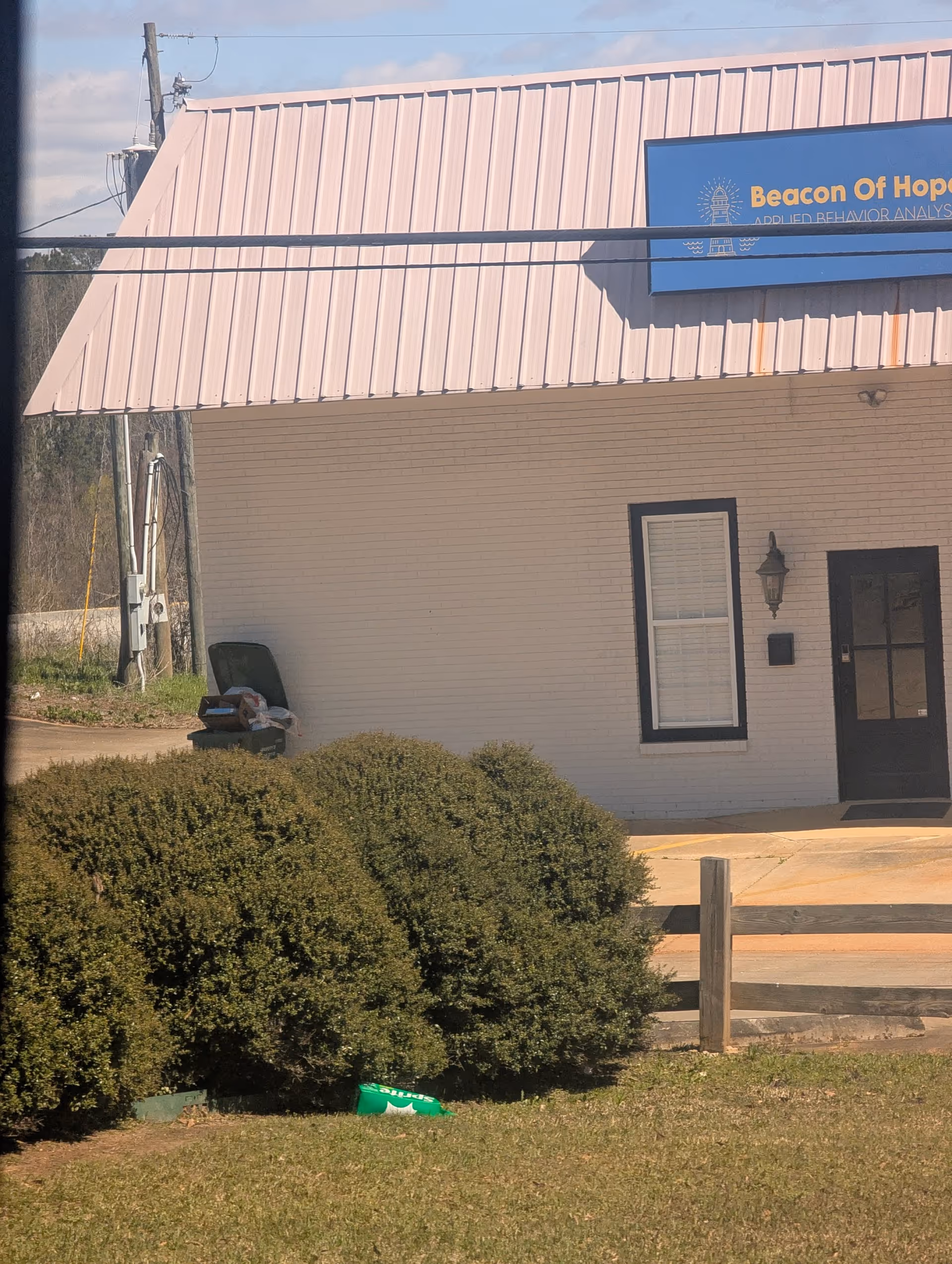 Exterior view of a small facility building with a pink metal roof and blue sign.