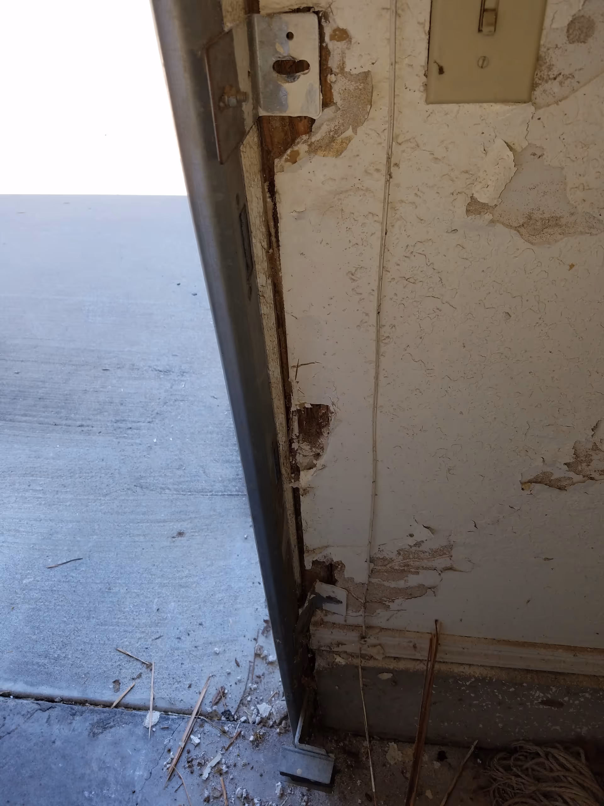A deteriorated doorway frame with peeling paint, exposed plaster, and debris inside.