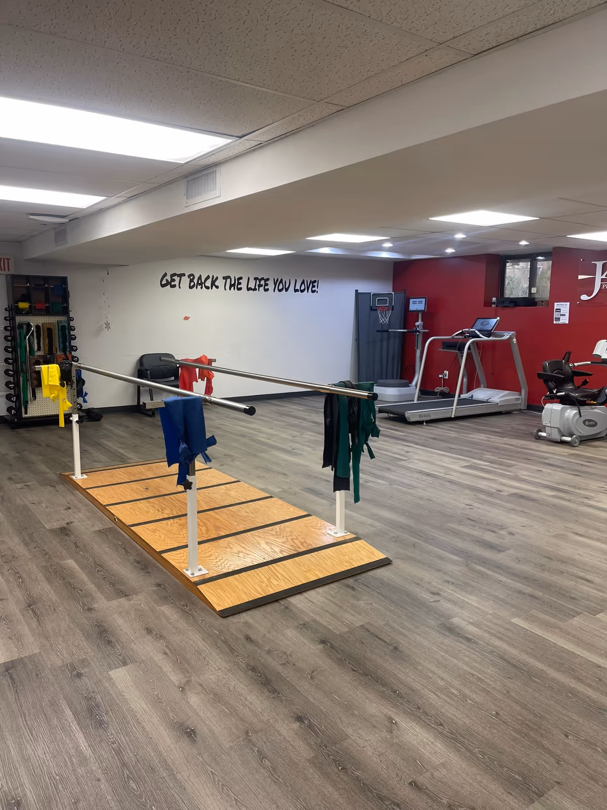 Indoor rehabilitation gym with parallel bars, cardio equipment, and motivational wall text.
