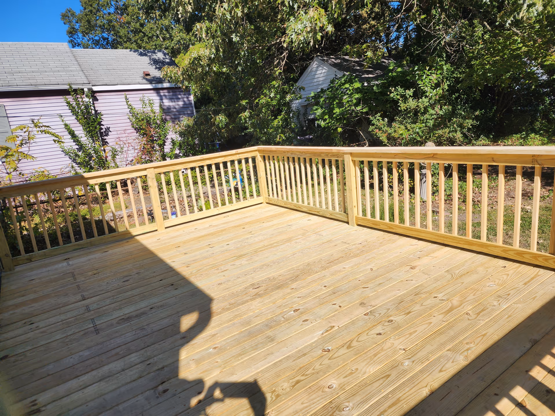 A wooden outdoor deck with railing sits beside trees and a neighboring house.
