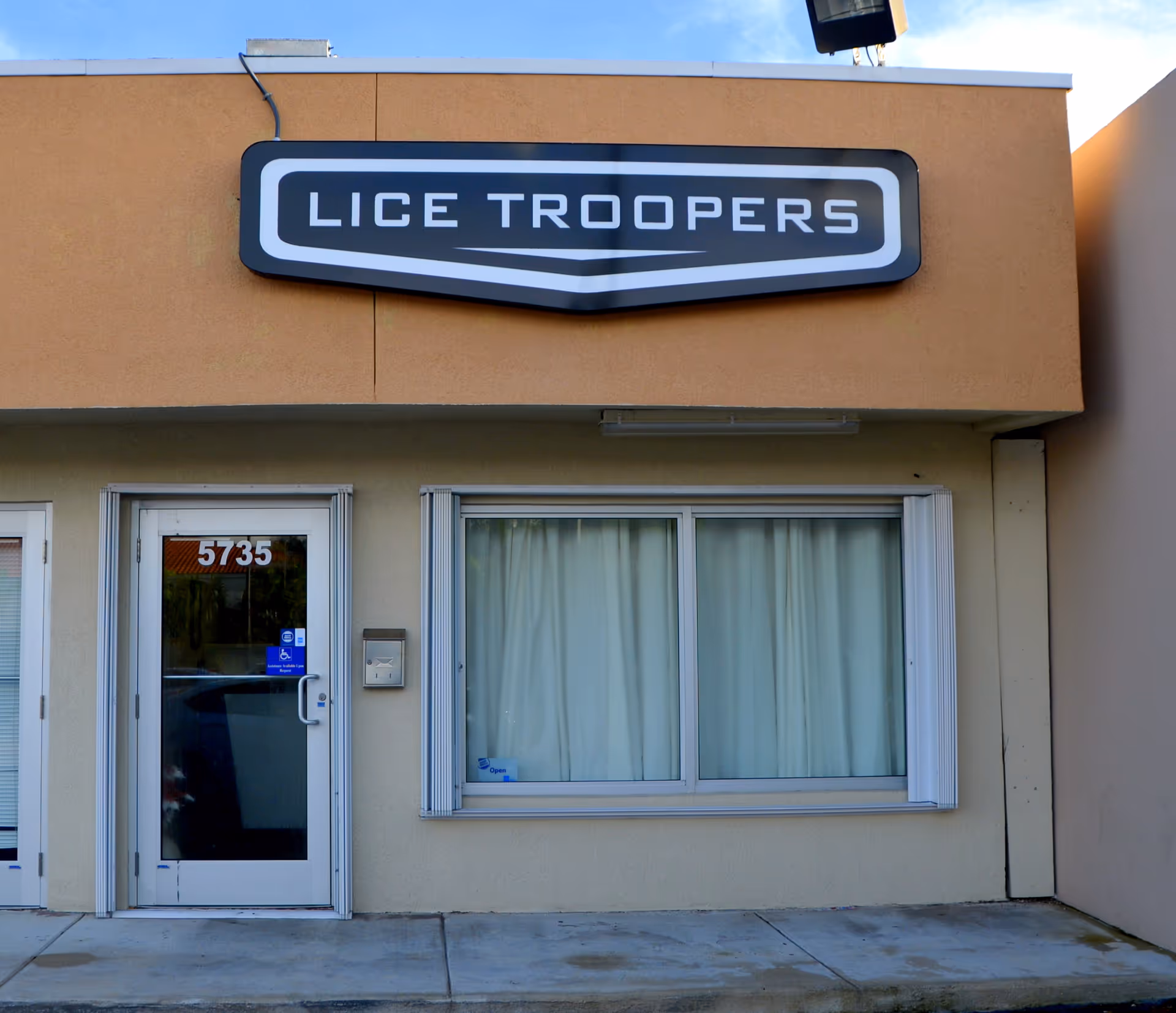 Front of a beige building with a 'Lice Troopers' sign above doors and window.