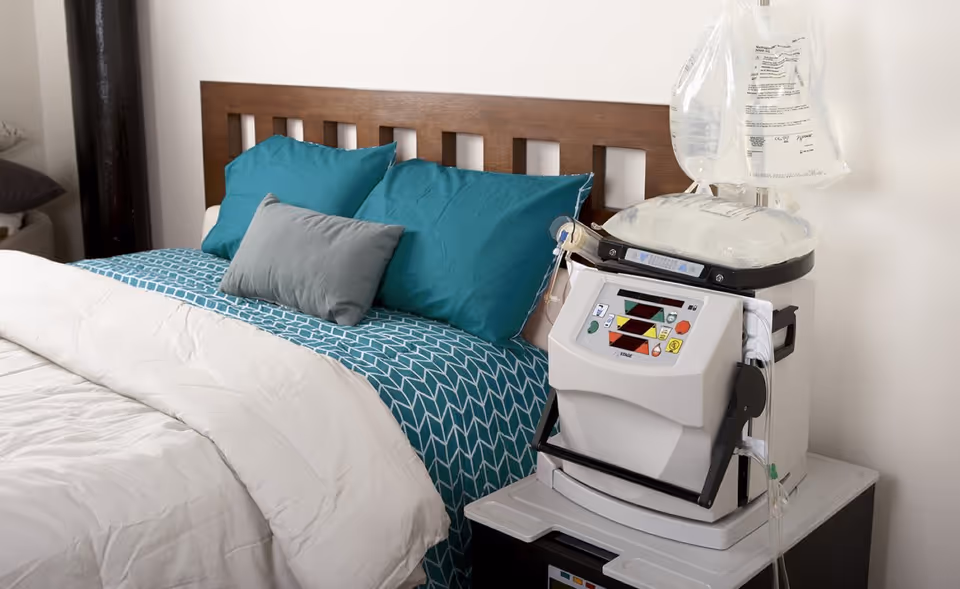 A bedroom with a wooden headboard, teal pillows, and a medical device on a nightstand.