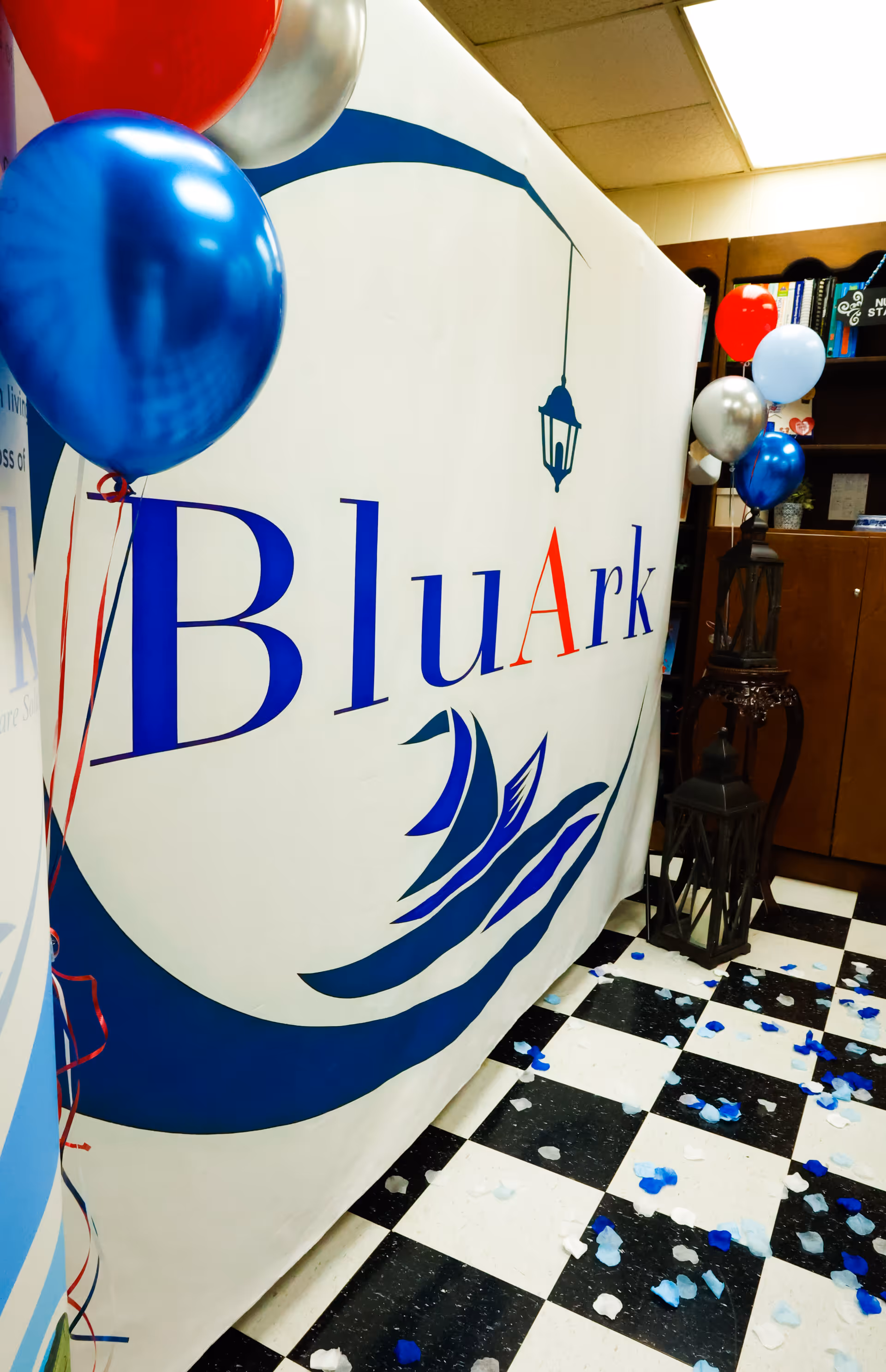 Large BluArk banner with blue balloons in an indoor checkered lobby.