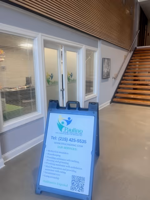 Interior hallway at Paulino Home Healthcare with glass doors and a blue information sign.