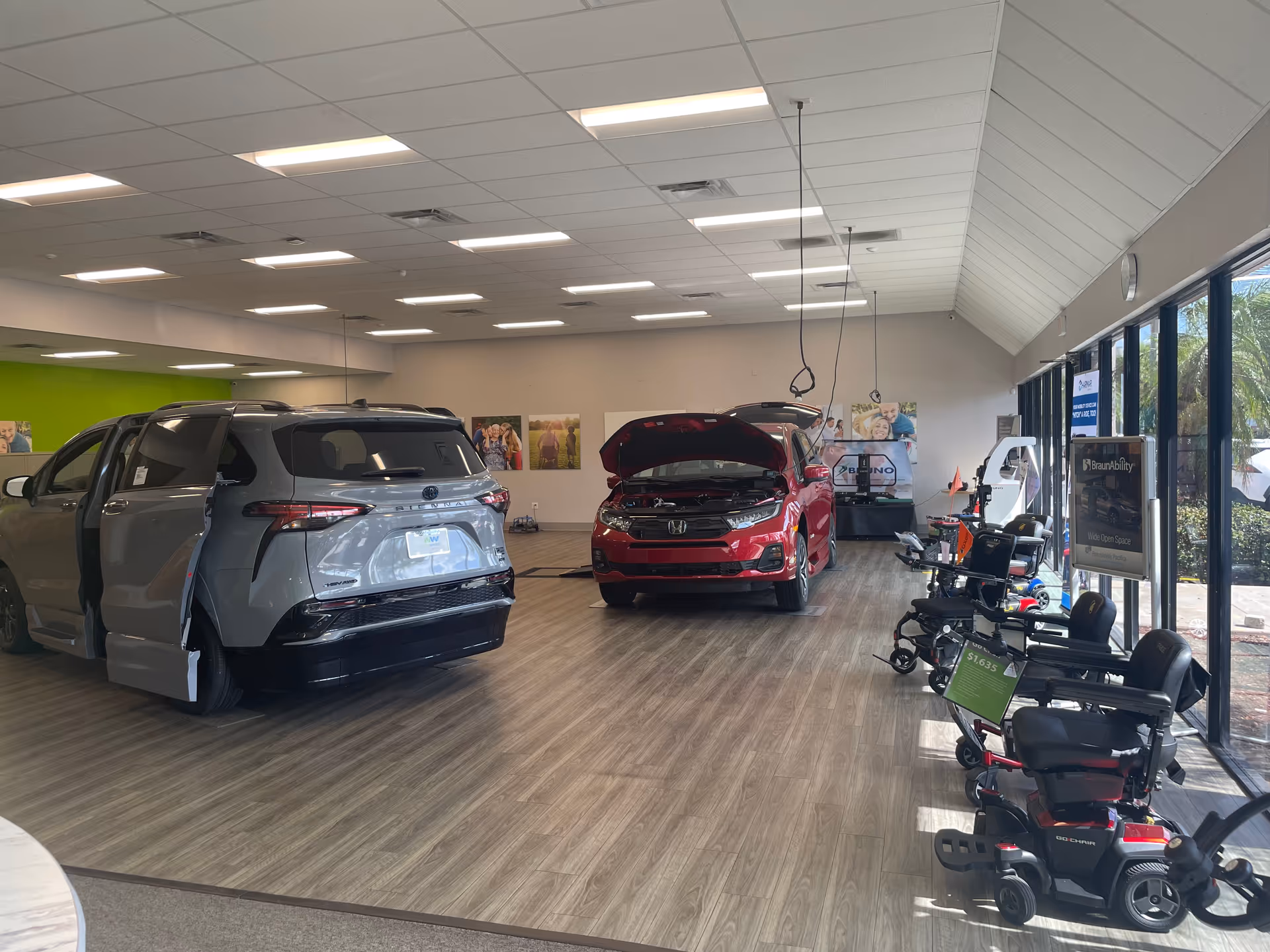 Indoor showroom with two cars and mobility scooters on display.