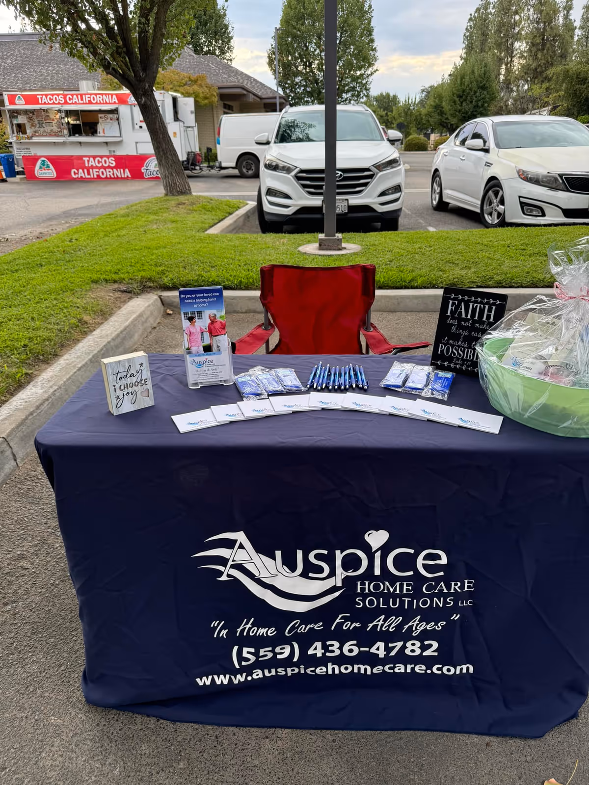 Outdoor promotional table for Auspice Home Care Solutions with brochures in a parking lot.