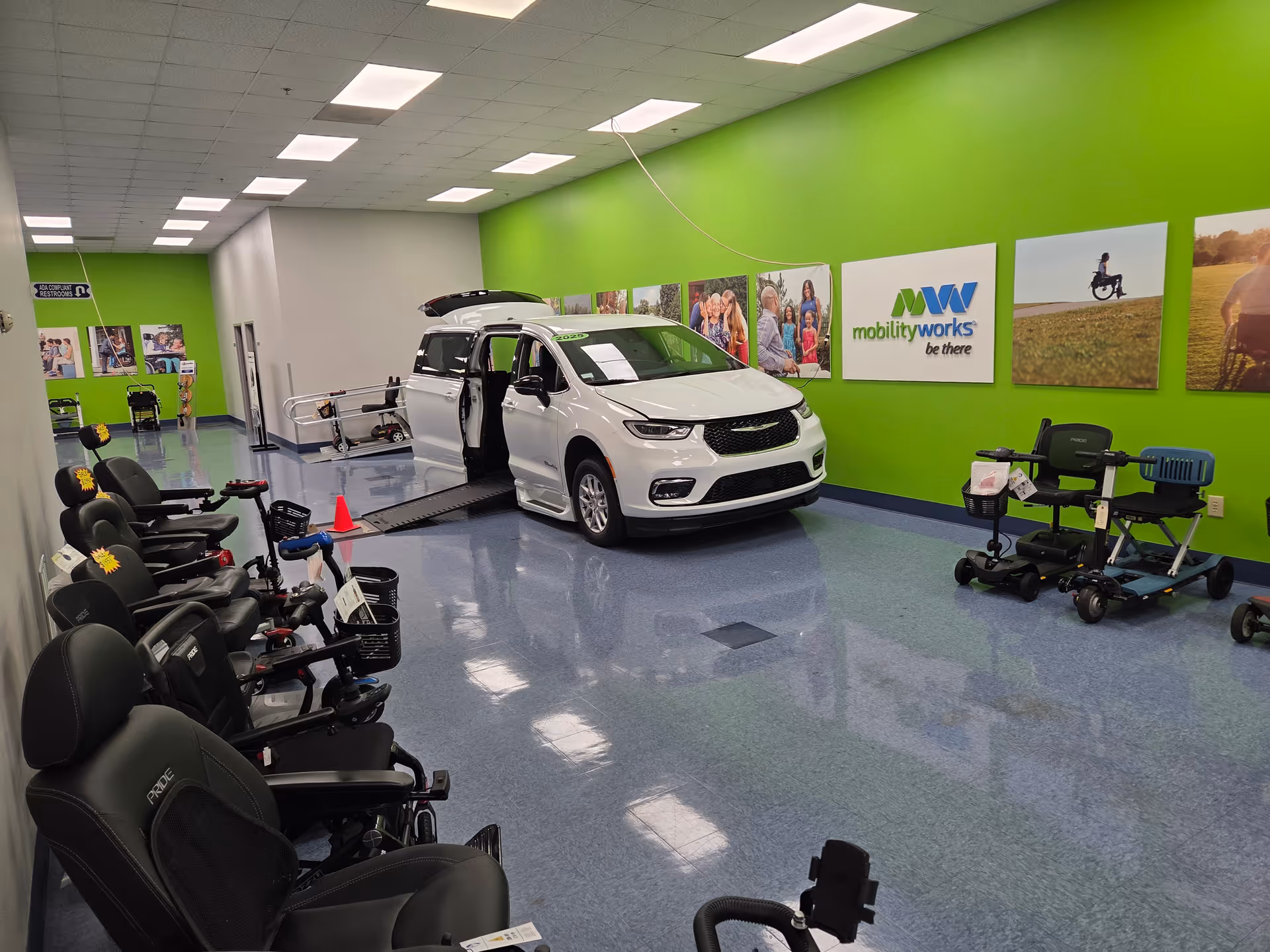 White van with ramp in a bright green interior showroom, surrounded by mobility chairs and equipment.
