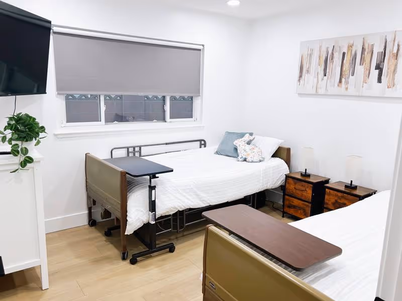 Bright white patient bedroom with two single beds, a window, nightstands, and wall art.