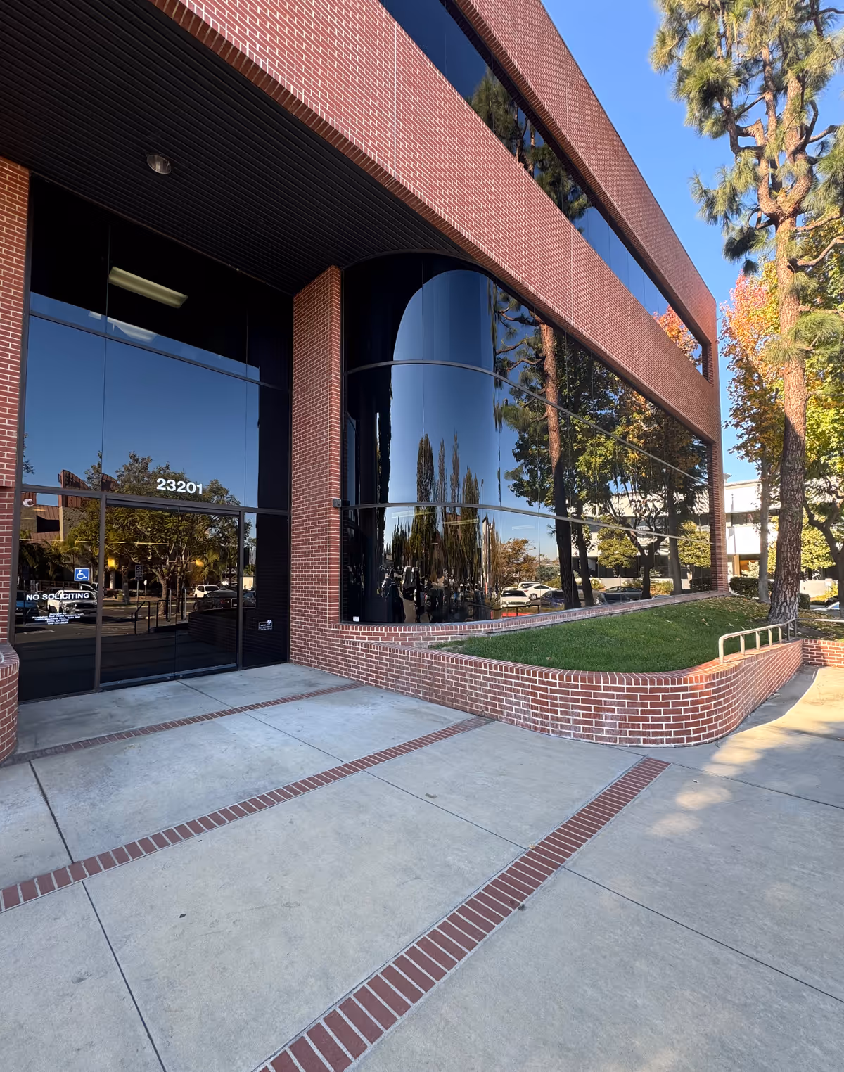 Front view of a brick building entrance with curved glass windows and a wide sidewalk.