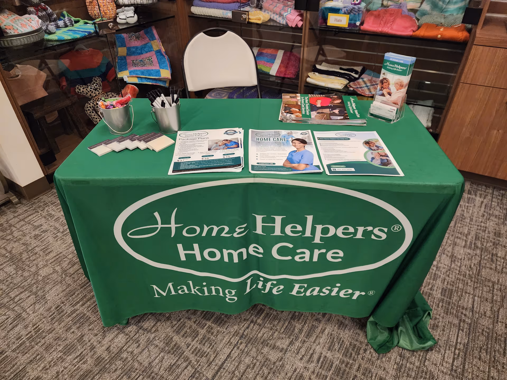 Green table with Home Helpers Home Care brochures and supplies in a facility lobby.