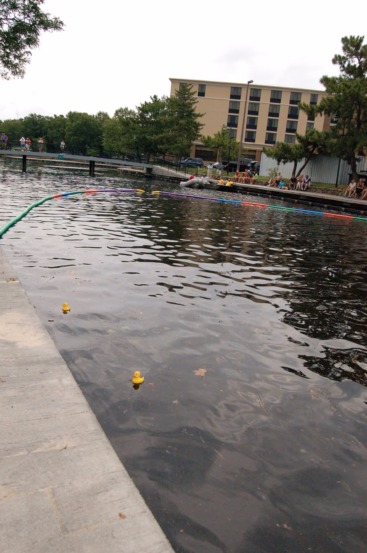 Outdoor waterfront area beside a tan multi-story building with a boardwalk and people.