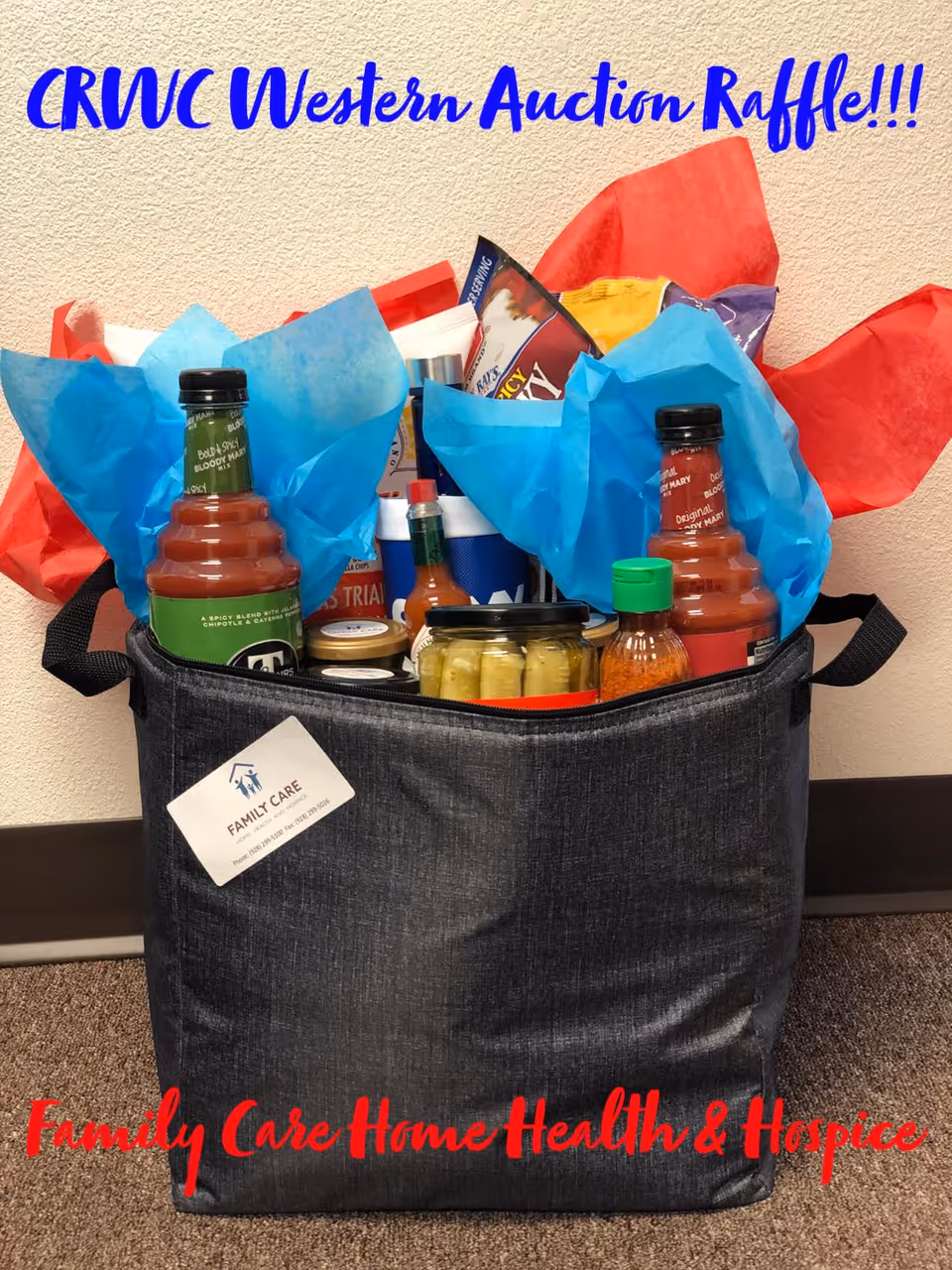 A dark fabric tote filled with sauces and snacks sits on a carpeted floor indoors.