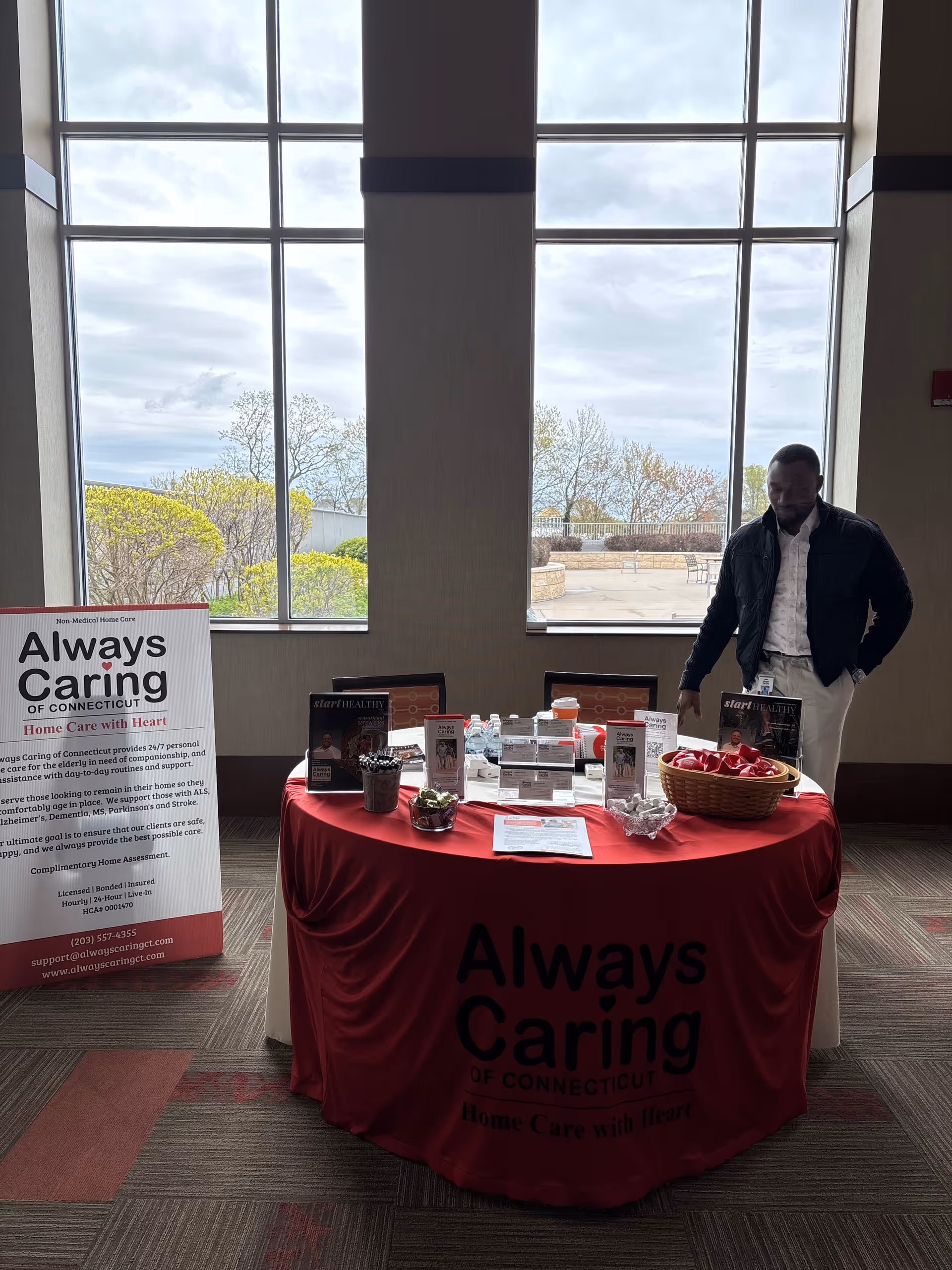 Indoor lobby with a red tablecloth, promotional banners, and a man near large windows.