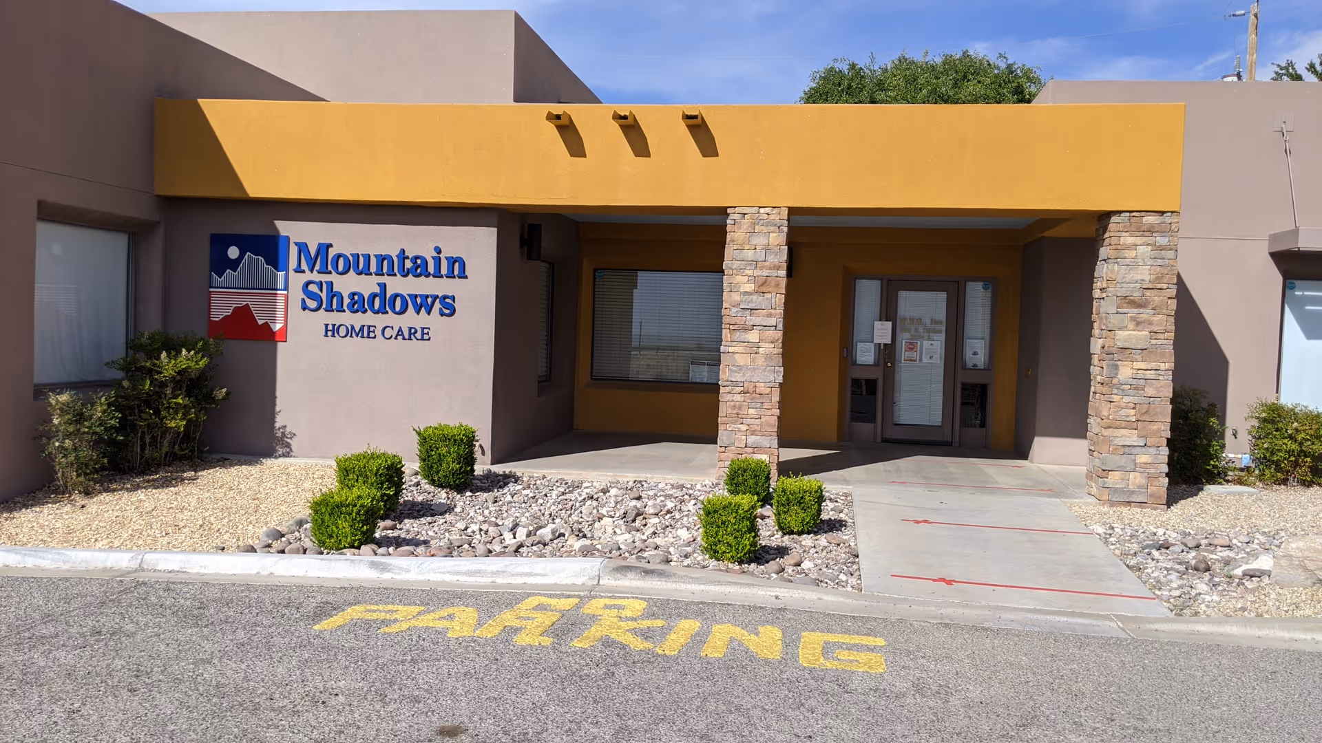 Exterior view of Mountain Shadows Home Care with entrance, sign, stone columns, and xeriscape landscaping.
