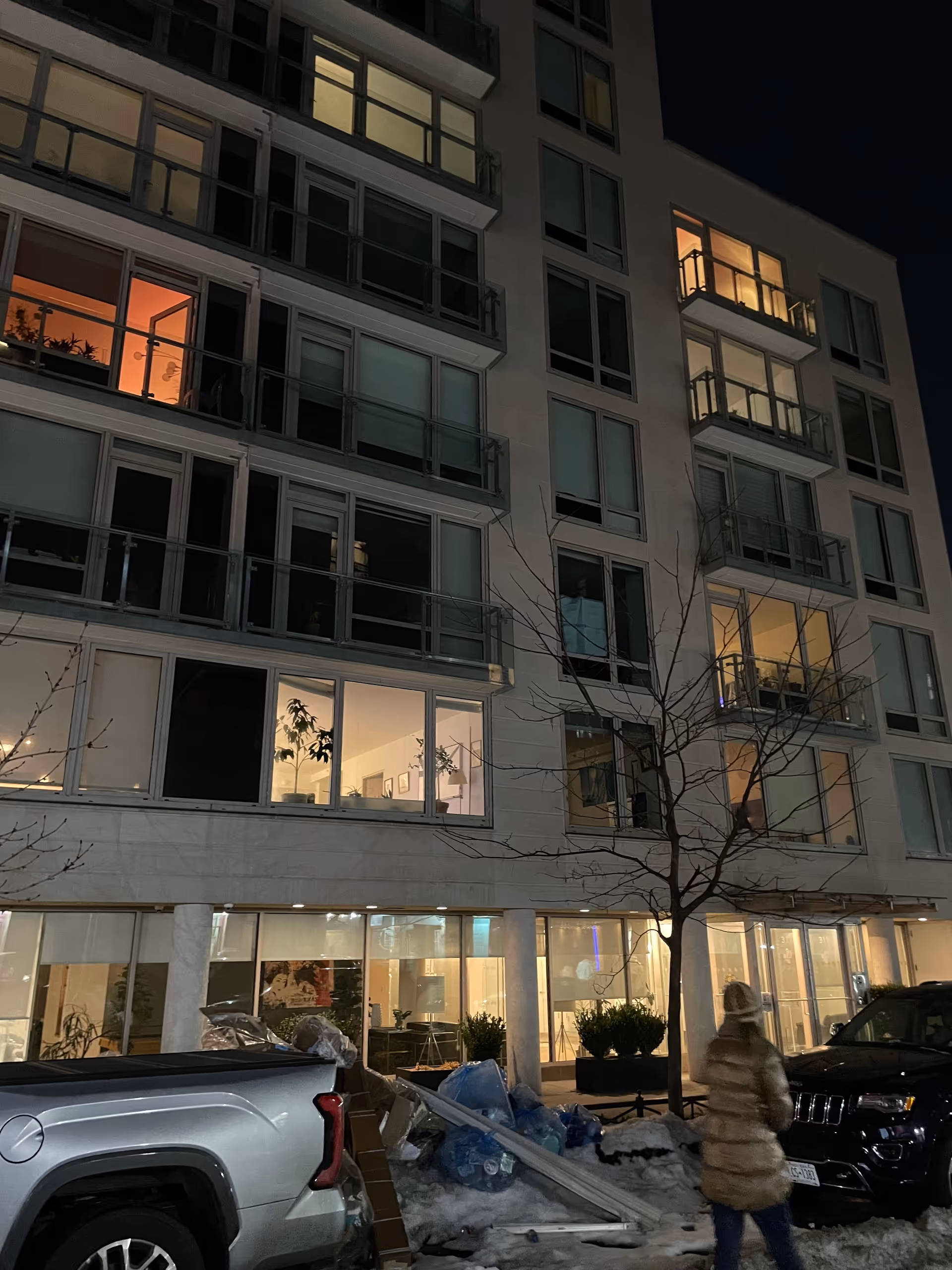 Nighttime exterior view of a multi-story senior living building with lit windows and parked cars.