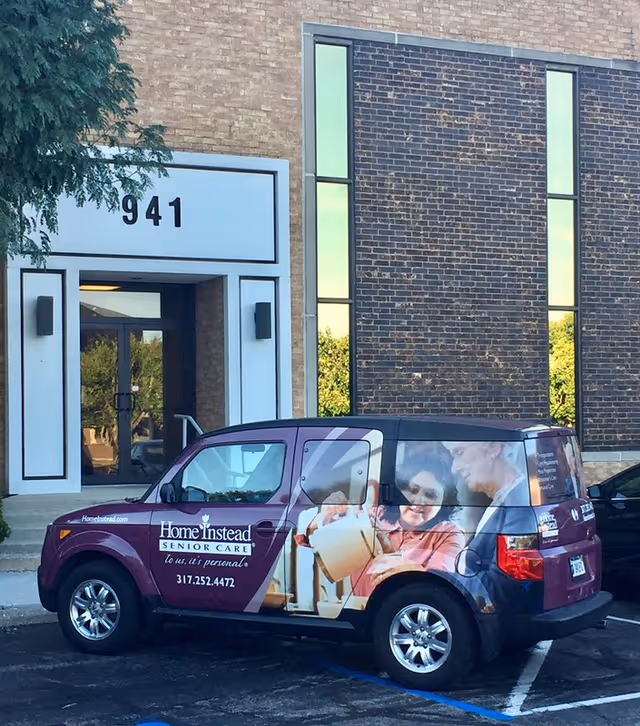 Maroon Home Instead Senior Care van parked in front of a brick building entrance.