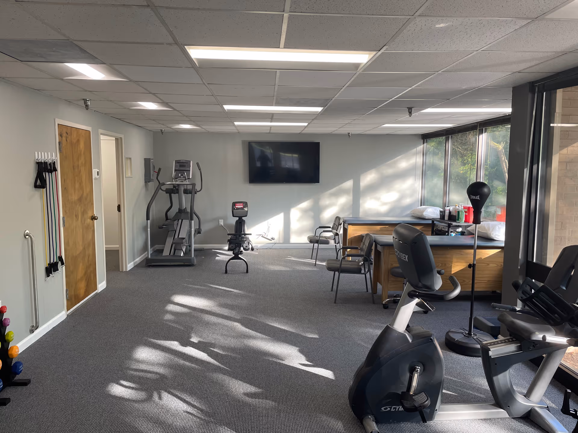 Indoor fitness room at ACES HOME HEALTH with treadmill, bike, weights, and windows.