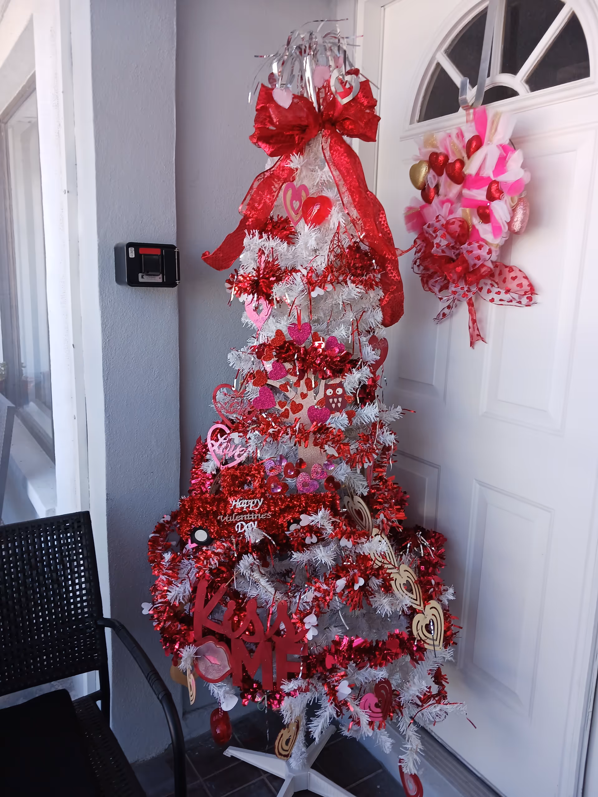 Valentine-themed white artificial tree with red decorations sits by a front door on a porch