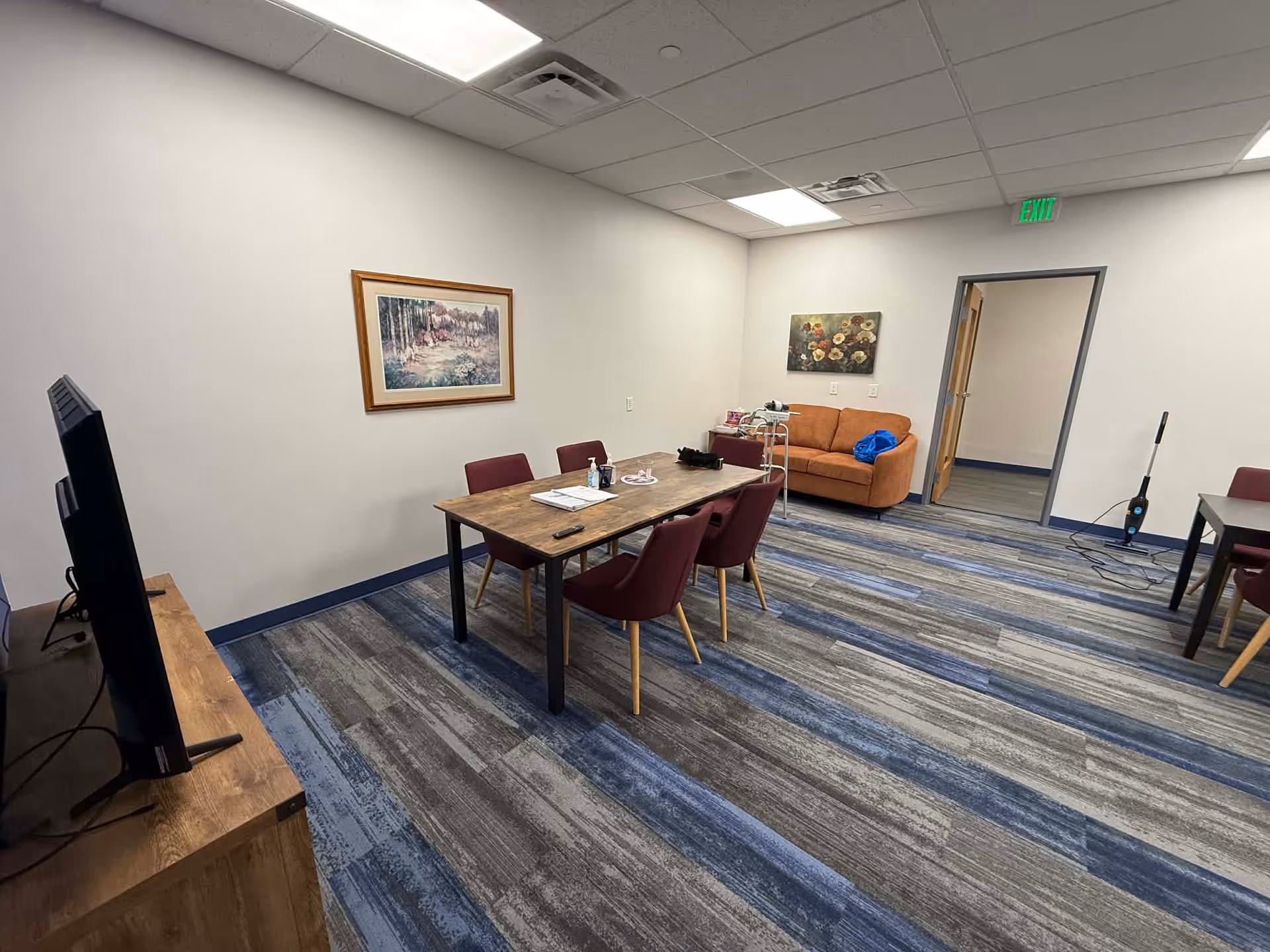 A senior living common area with a dining table, chairs, couch, and a TV.