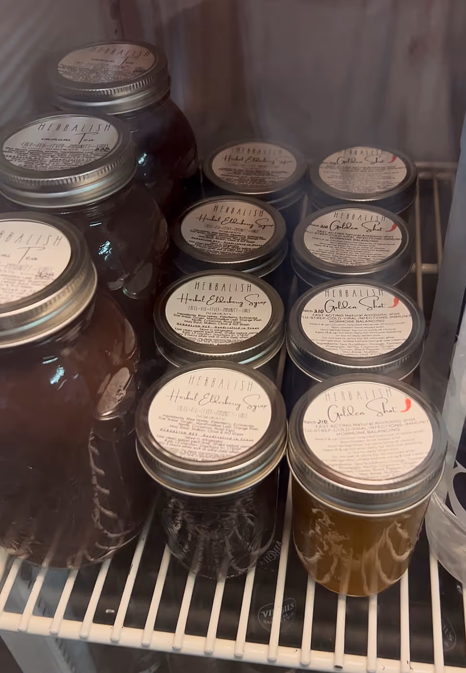 Row of glass jars labeled Herbalish on a fridge shelf in a kitchen