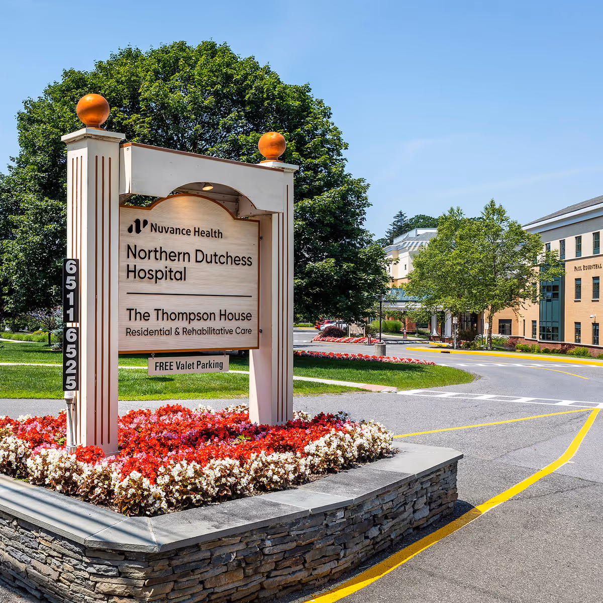 Nuvance Health hospital campus sign with landscaped flowers and a building in the background.