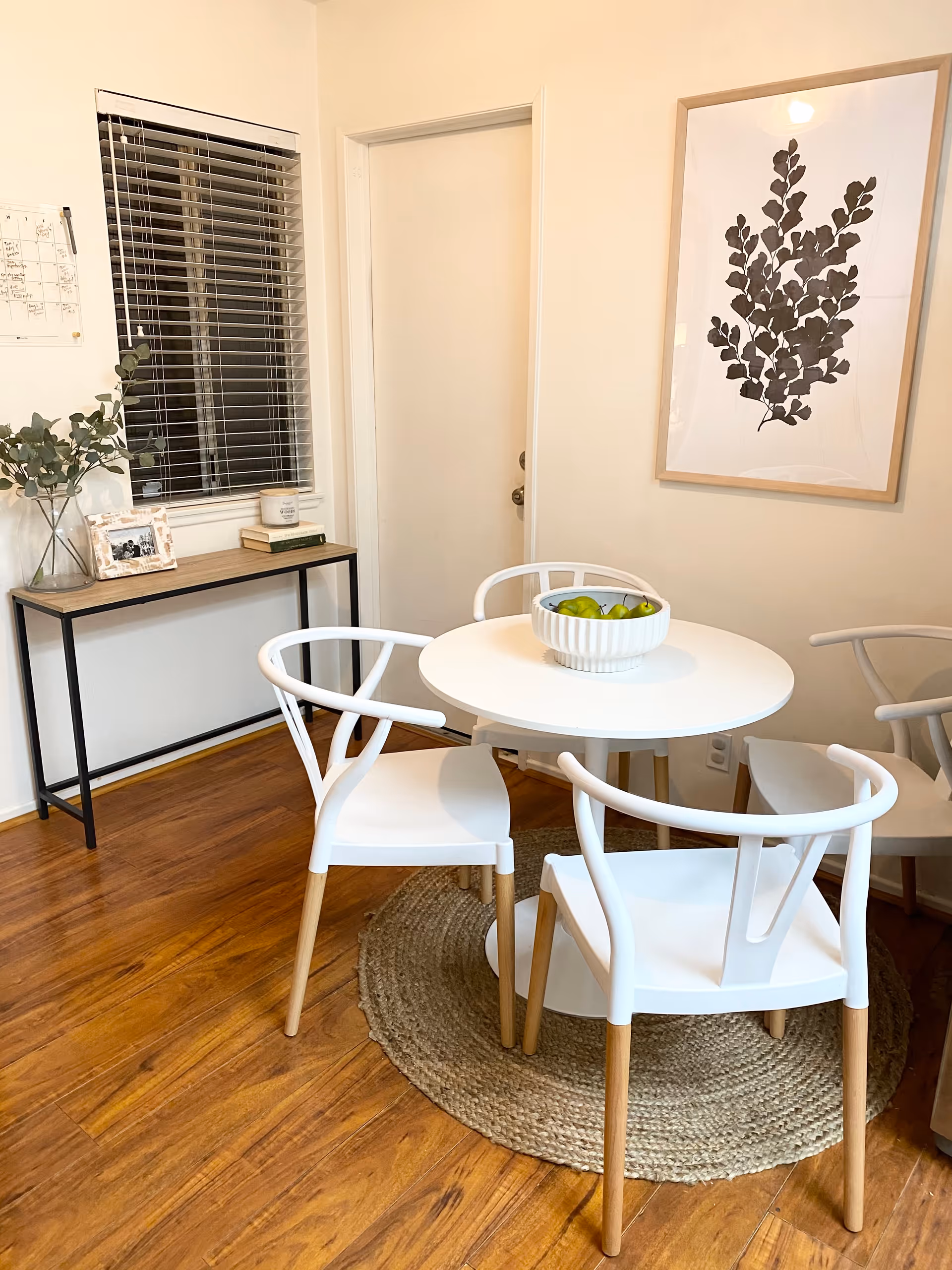 White round table with four white chairs in a cozy dining area with a round rug.