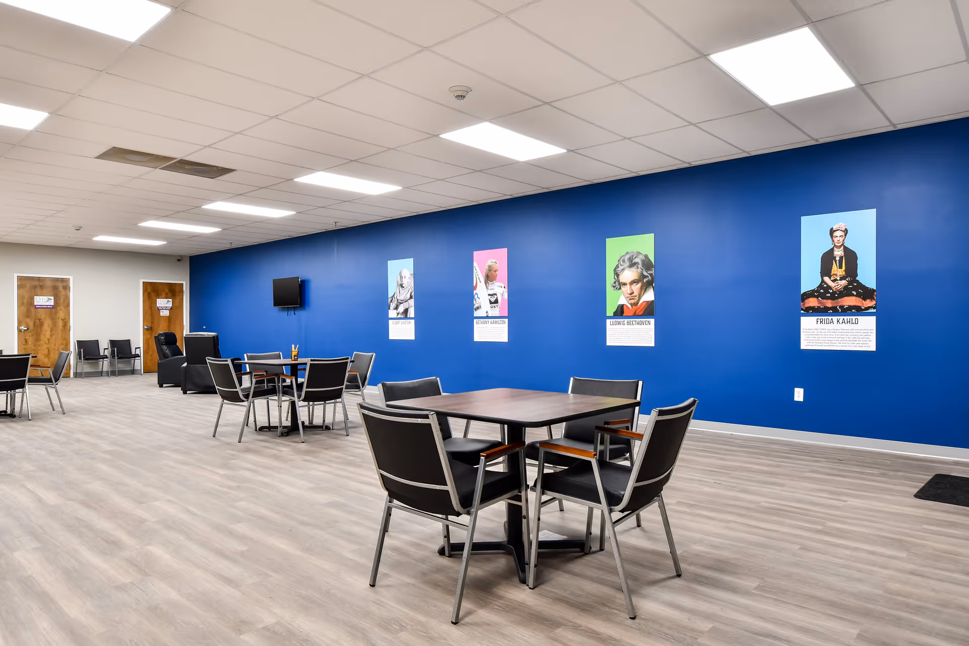 Spacious interior communal dining area with round tables, black chairs, and blue wall posters.