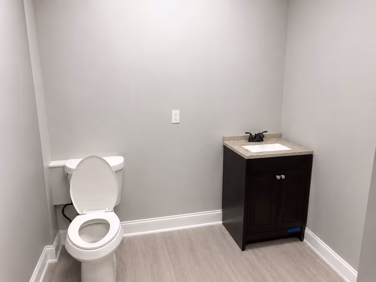 Small bathroom with toilet and dark vanity sink in a neutral room.