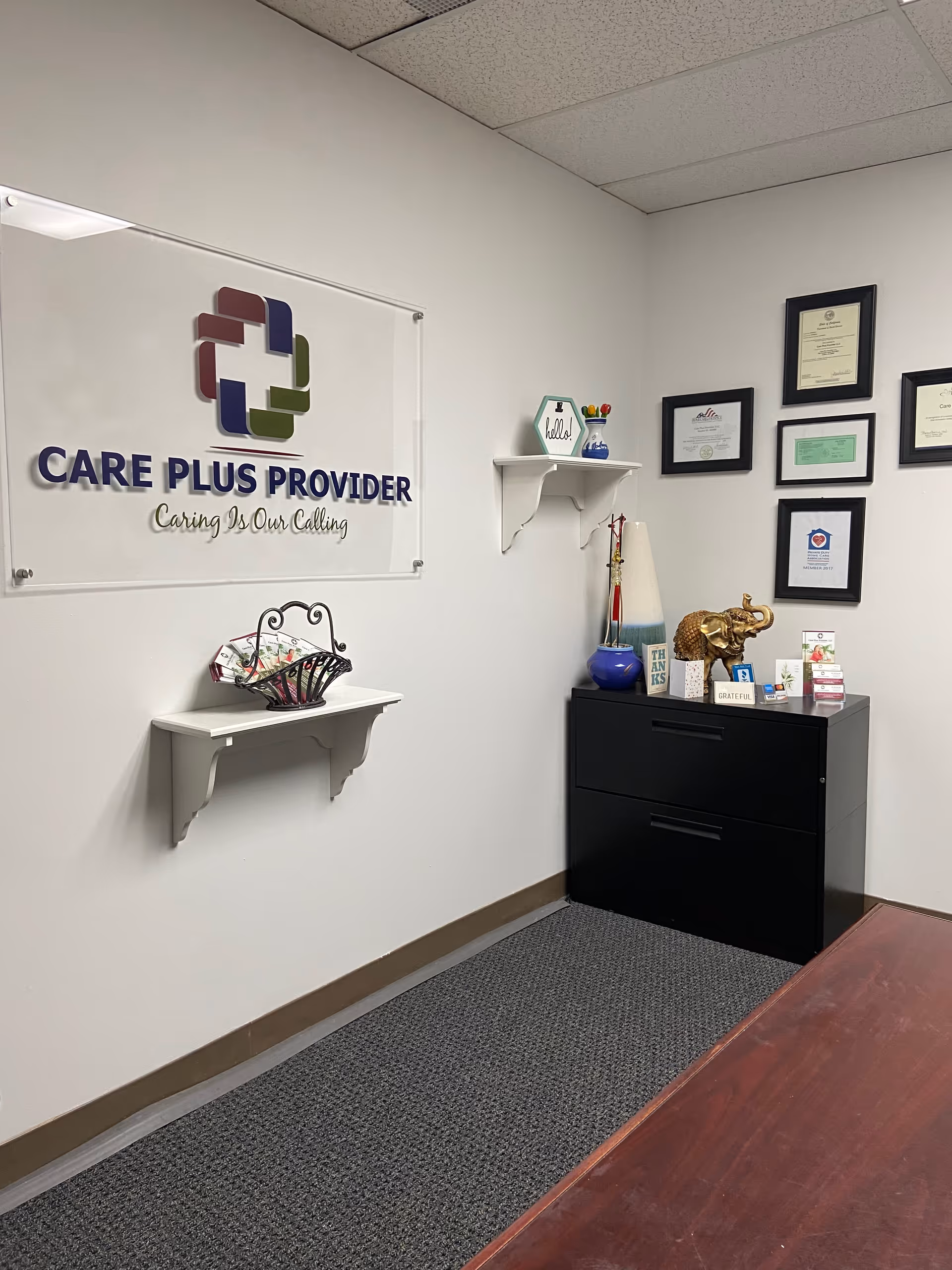 Reception area of Care Plus Provider with wall sign, certificates, shelf, and black cabinet.