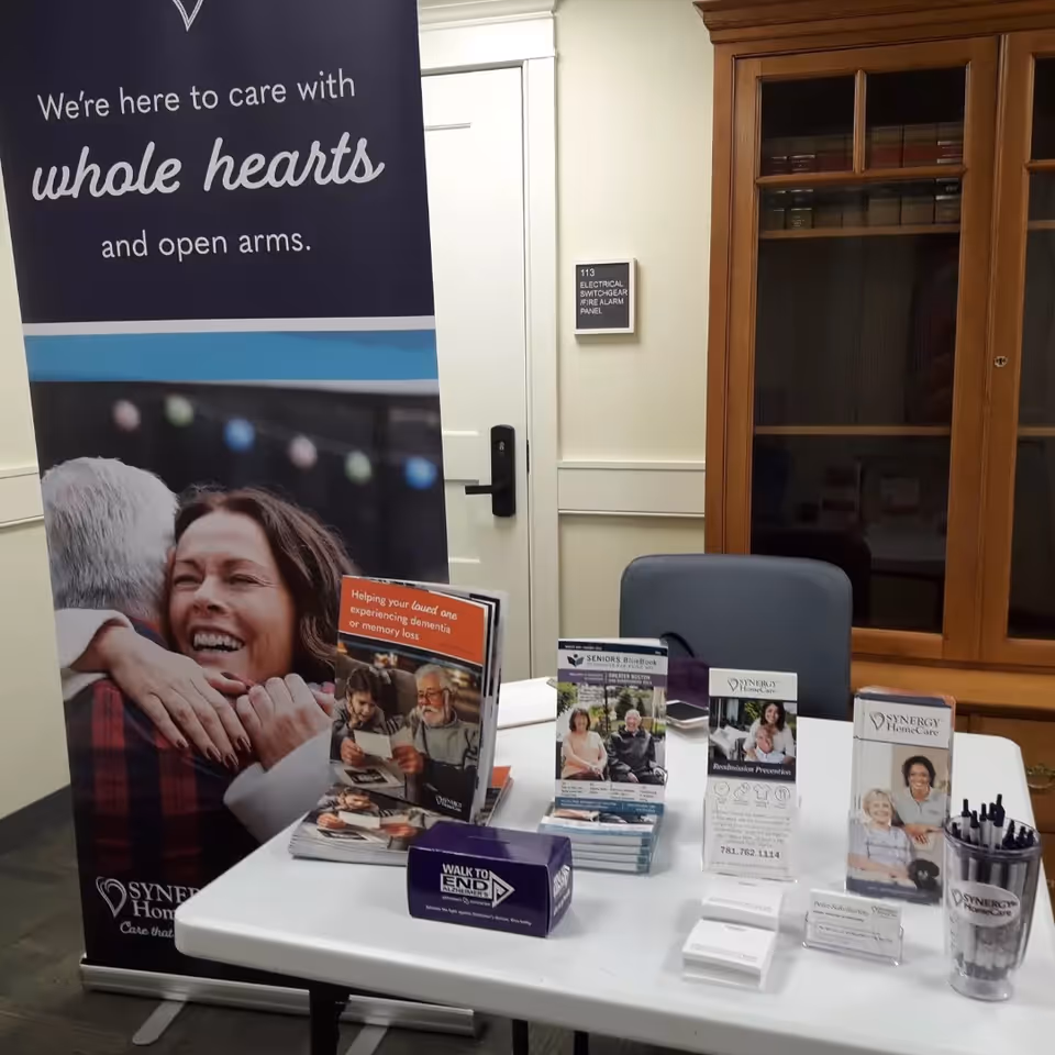 Promotional table with brochures and a SYNERGY HomeCare banner indoors