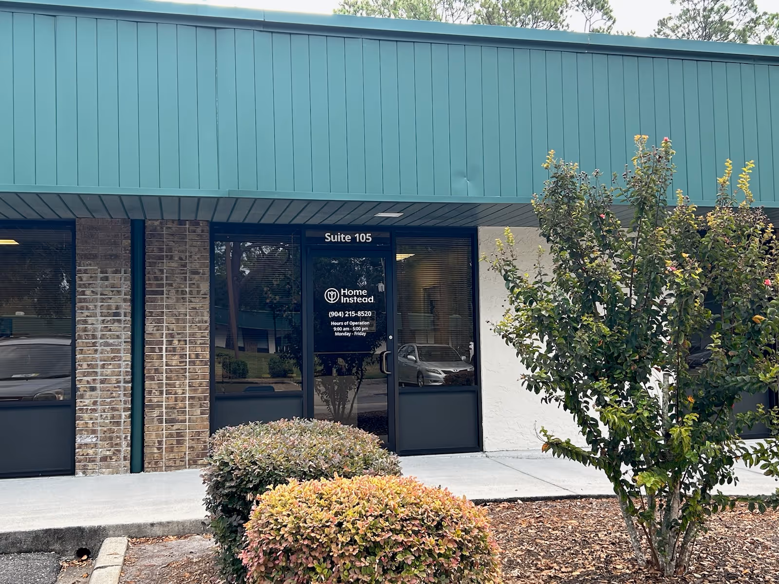 Exterior view of a Home Instead facility entrance with glass door and landscaping.