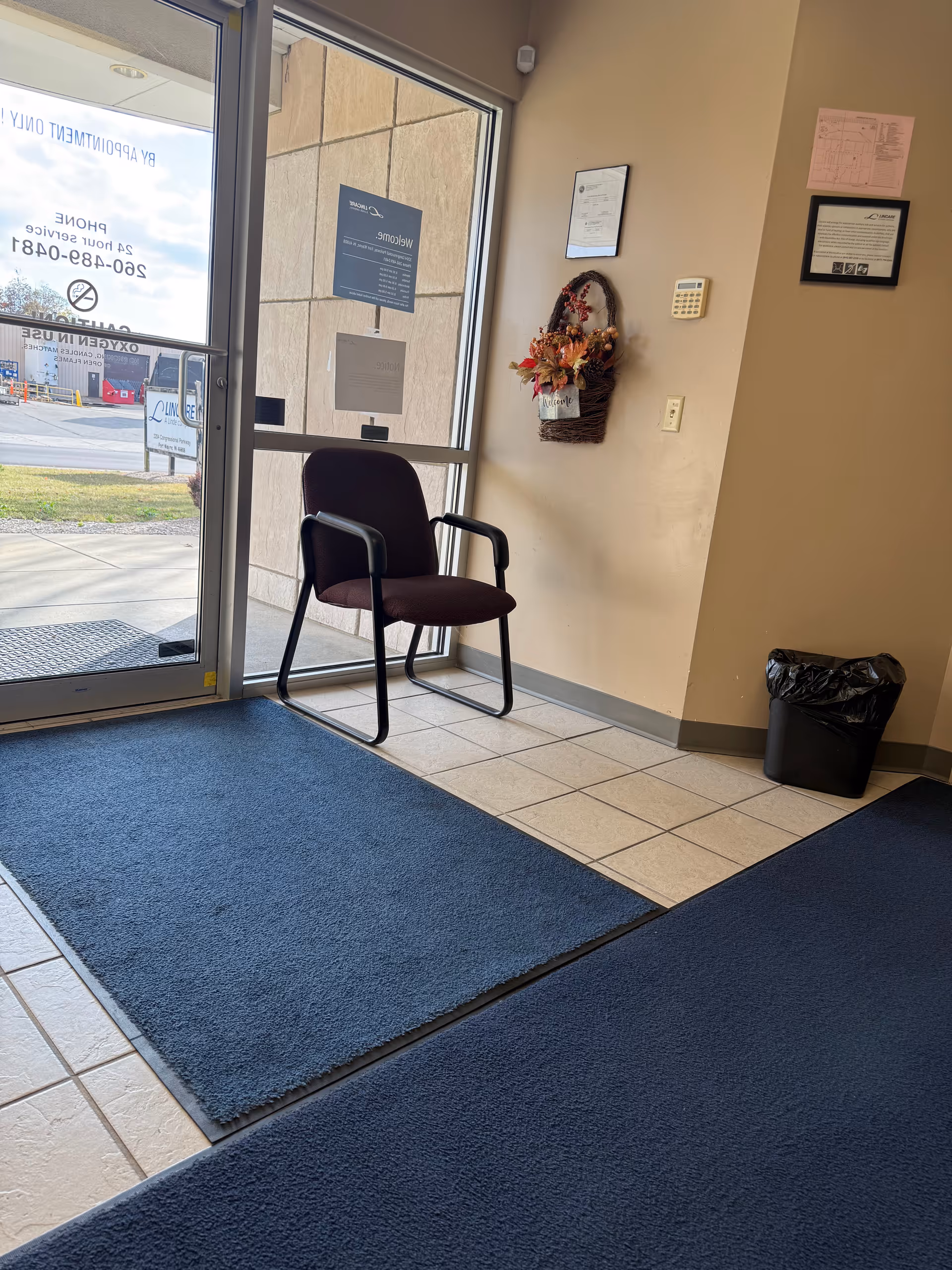 LINCARE lobby entrance with glass doors, blue floor mats, a chair, and wall decorations.