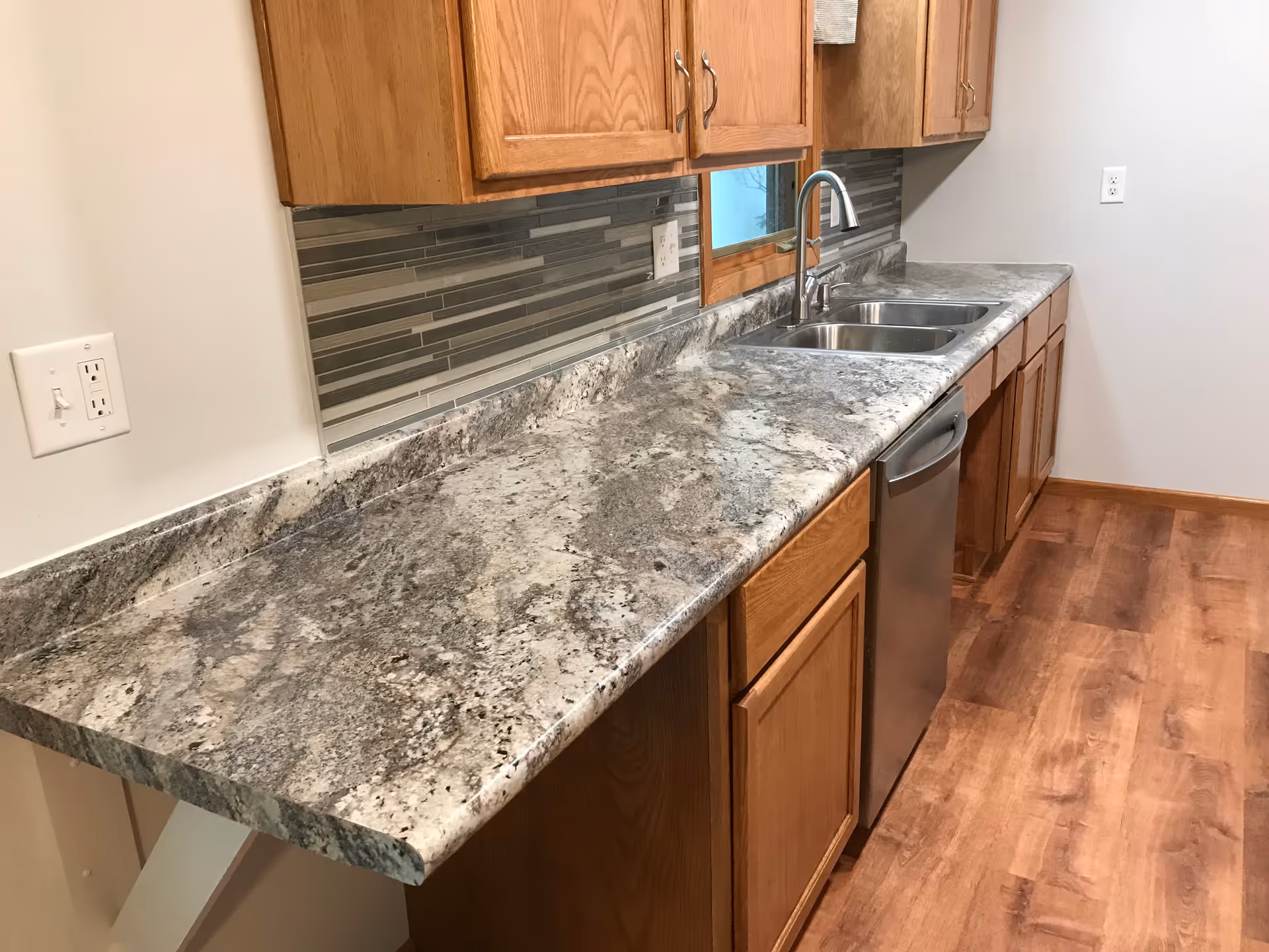 Clean kitchen with granite counters, wooden cabinets, tile backsplash, dishwasher, and sink.