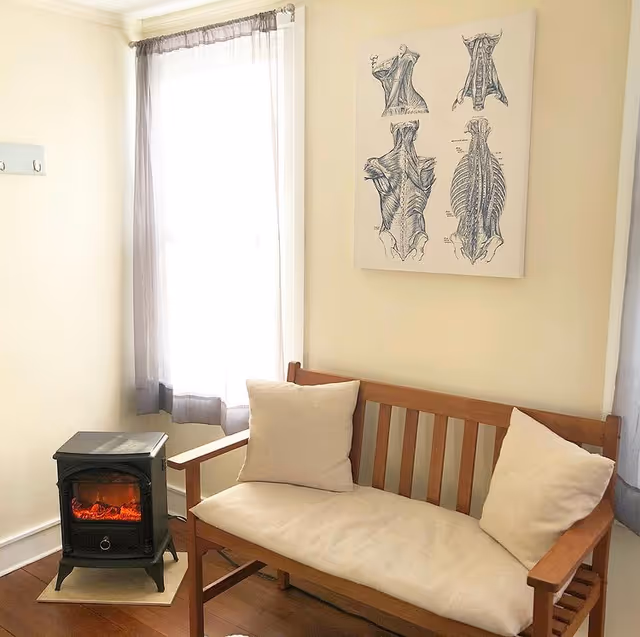 Wooden sofa with beige cushions beside a small electric heater and anatomy poster.