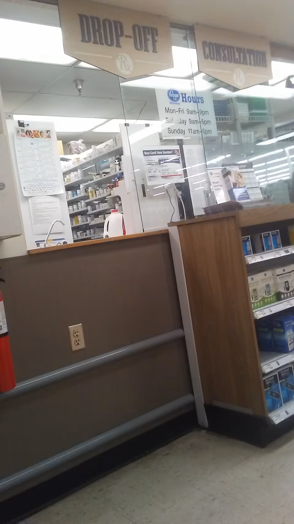 Kroger Pharmacy counter with drop-off and consultation signs behind glass shelving